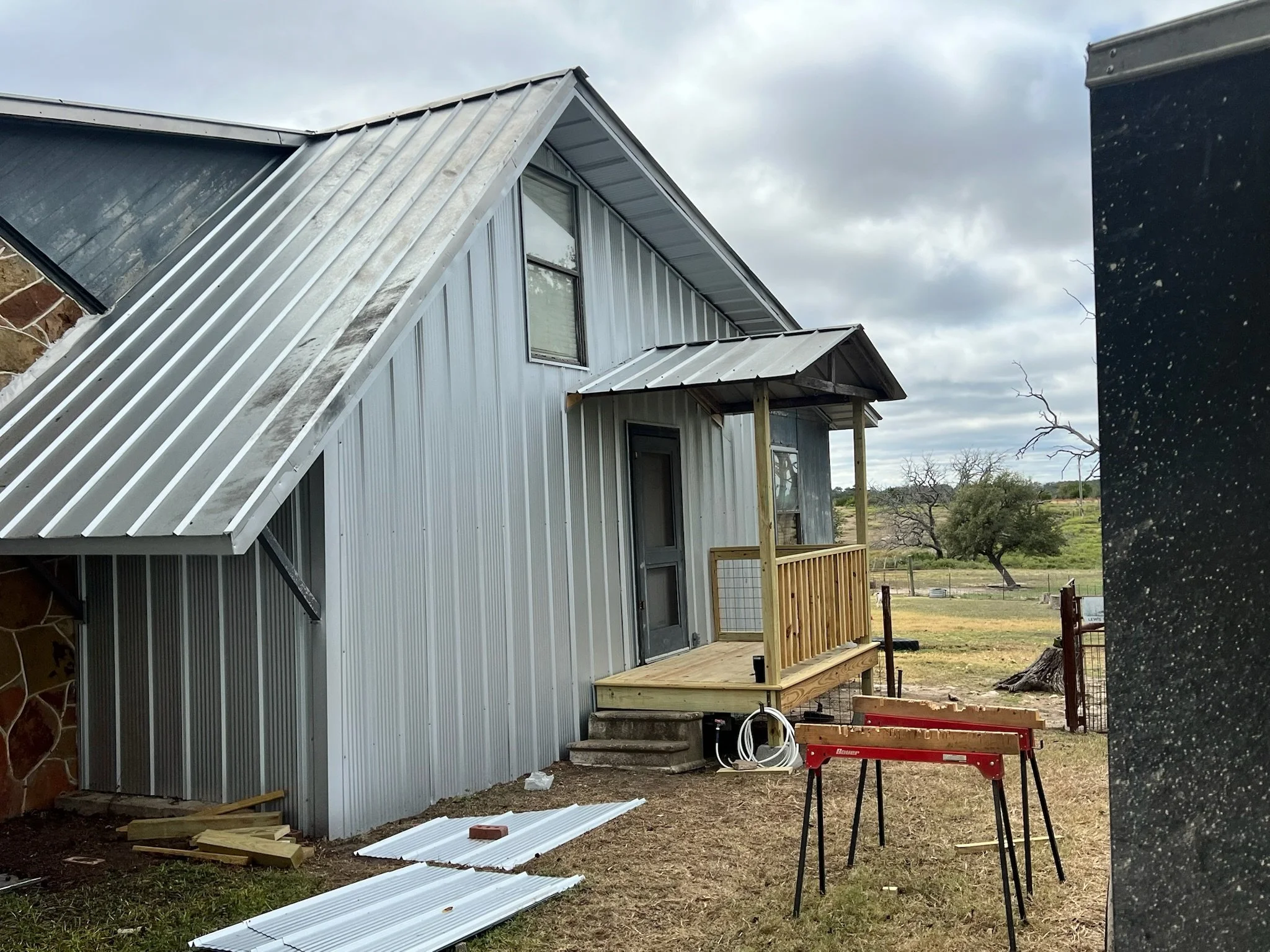 Side view of a house under construction with metal siding and roofing, with building materials and tools in the yard.