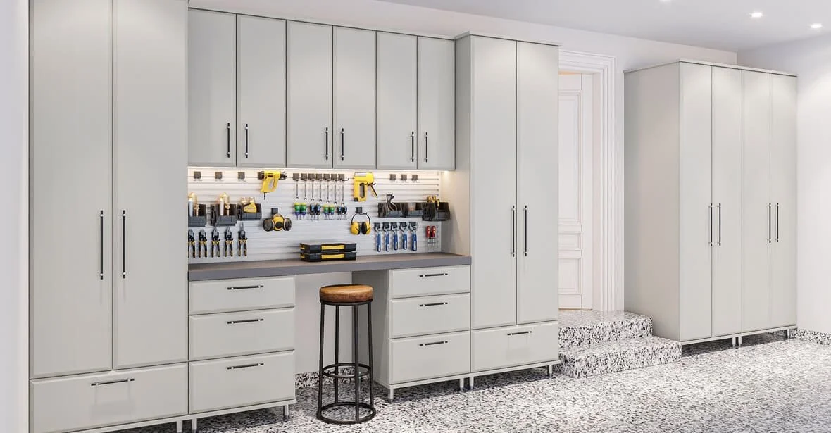 Garage storage area with white cabinets, a workbench with tools, and a stool, with a door and steps leading to another room.