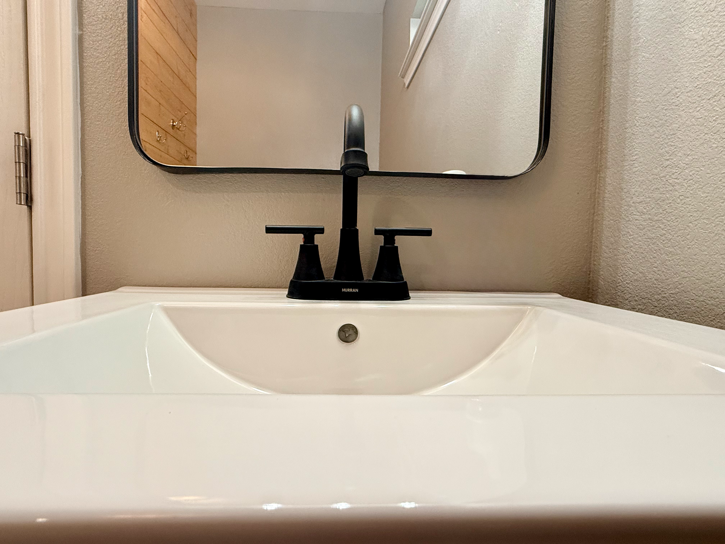 A bathroom sink with a black faucet, a round mirror mounted on the wall, and a reflection of a wooden cabinet with hooks on the wall.
