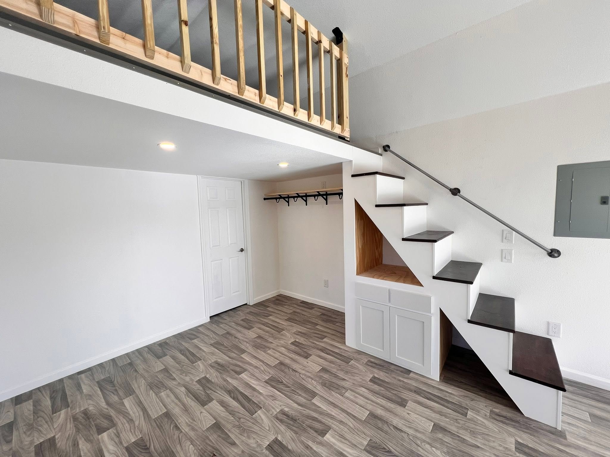 Interior of a modern house with a staircase, white walls, gray flooring, and a small balcony with wooden railing.