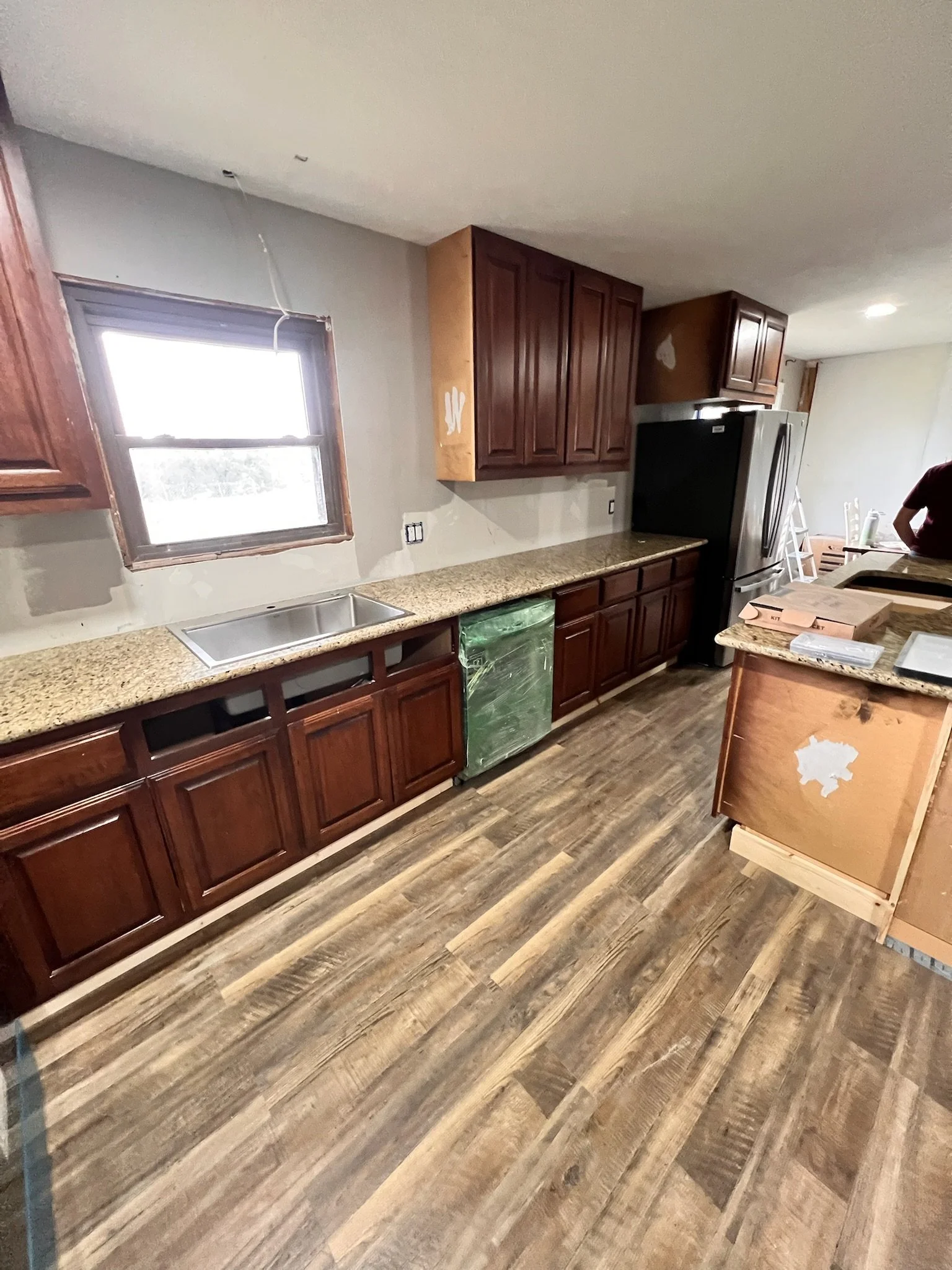 Kitchen with wooden cabinets, granite countertops, stainless steel sink, and a refrigerator; some cabinets are being painted or repaired.