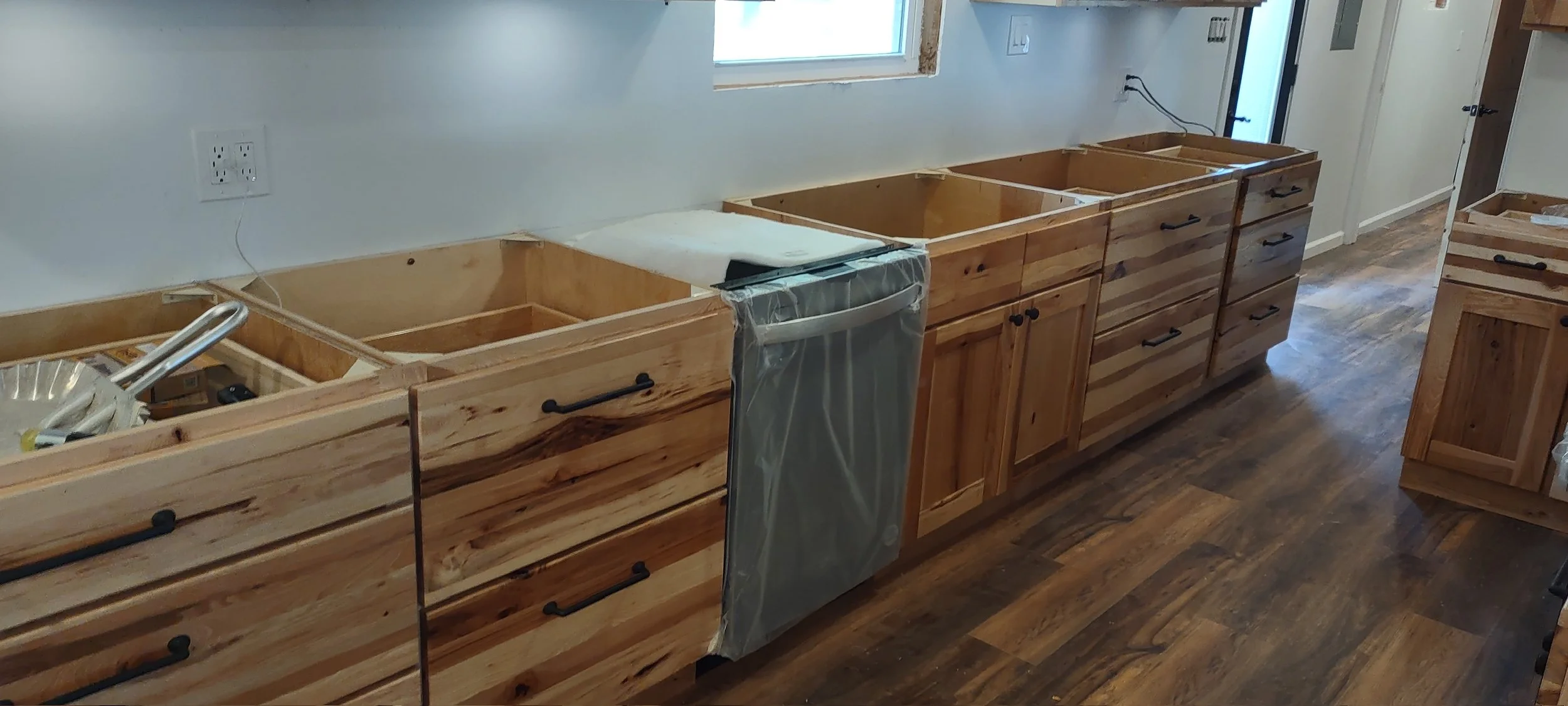 Kitchen cabinets under construction with unfinished wooden drawers and countertops, no appliances installed, and hardwood flooring.