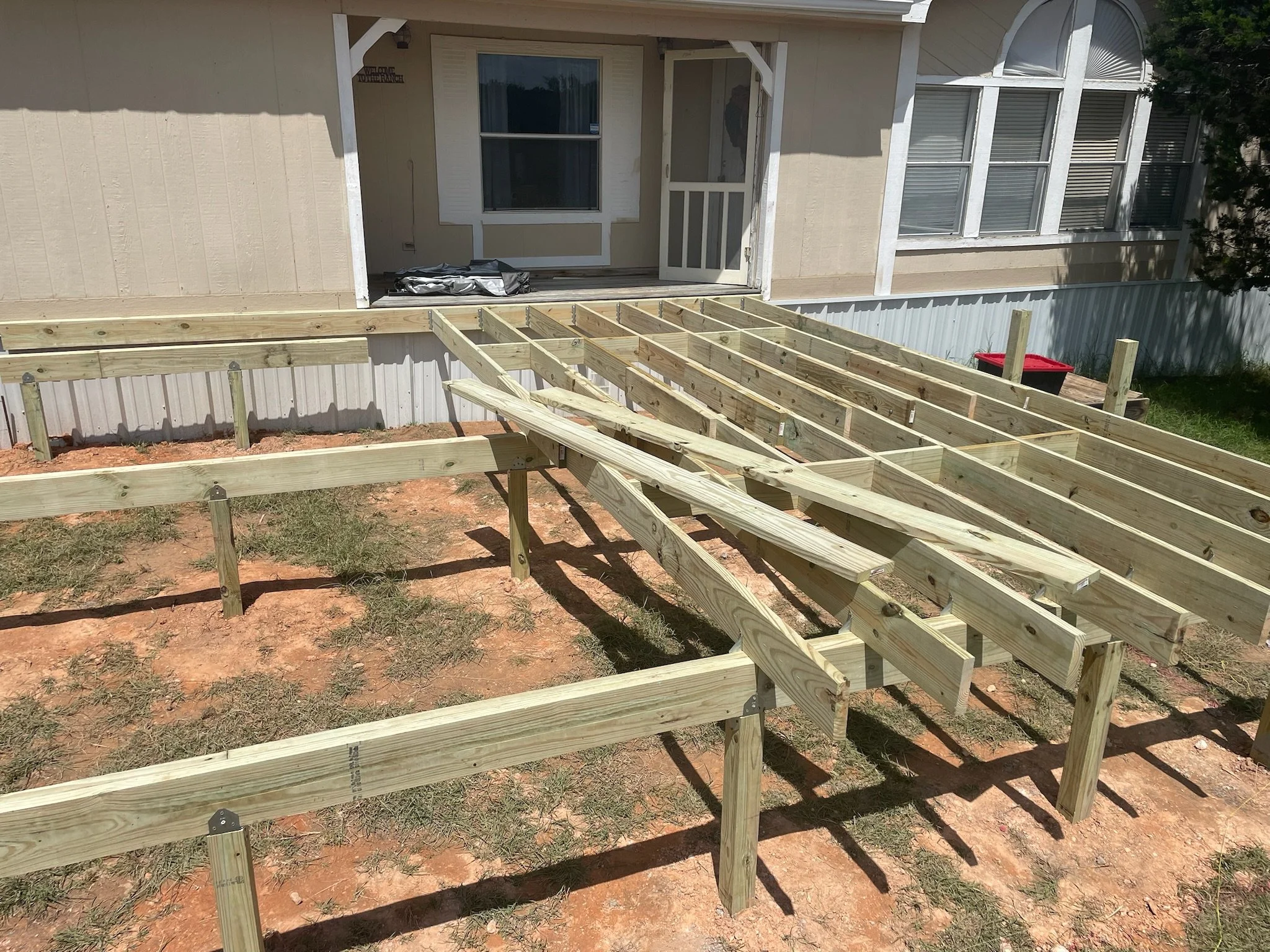 Wooden frame being built outside a house, with a sliding door and windows on the house's exterior wall.