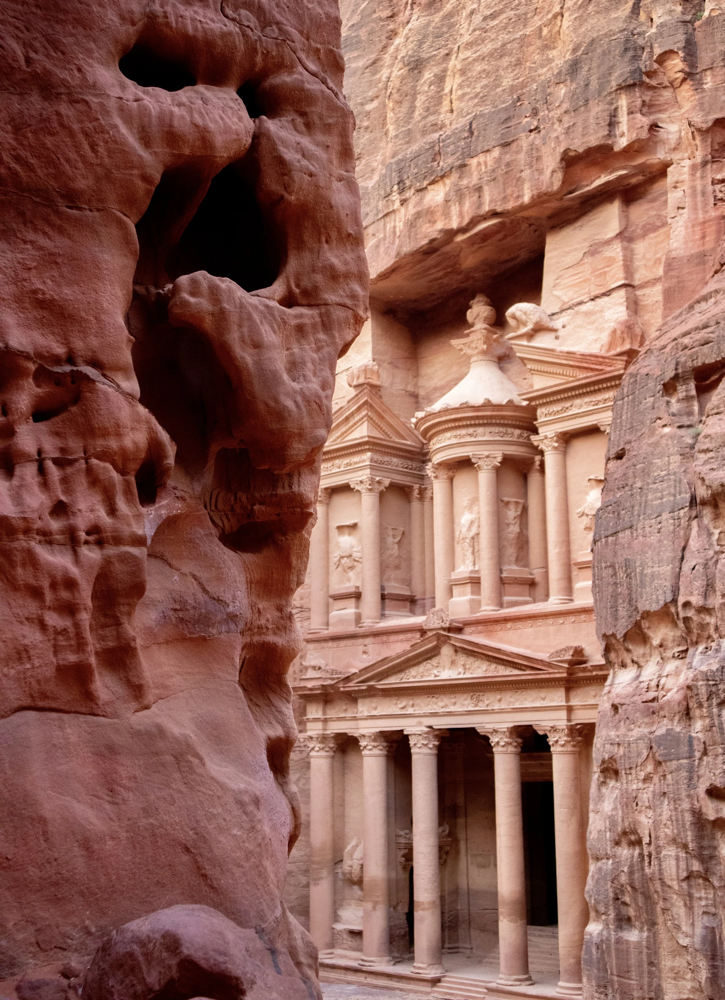 The image shows the historic Al-Khazneh, also known as The Treasury, carved into sandstone cliffs in Petra, Jordan, viewed through a narrow canyon.