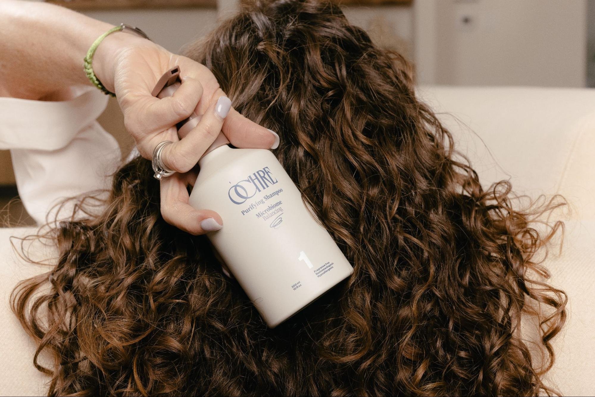 a woman with curly hair holding the best shampoos for hair loss