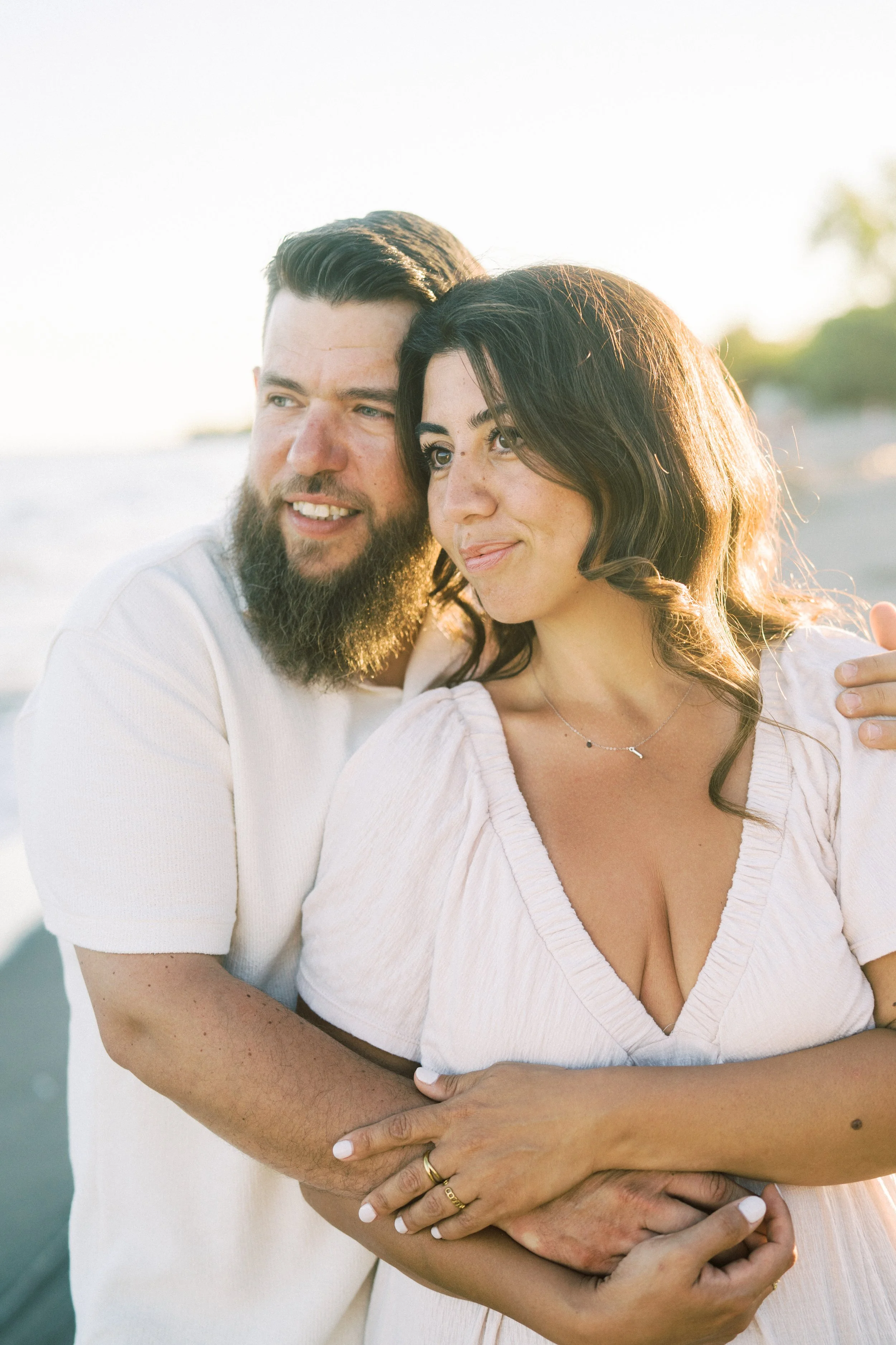 A happy couple is embracing on a beach during sunset, smiling and cuddling.