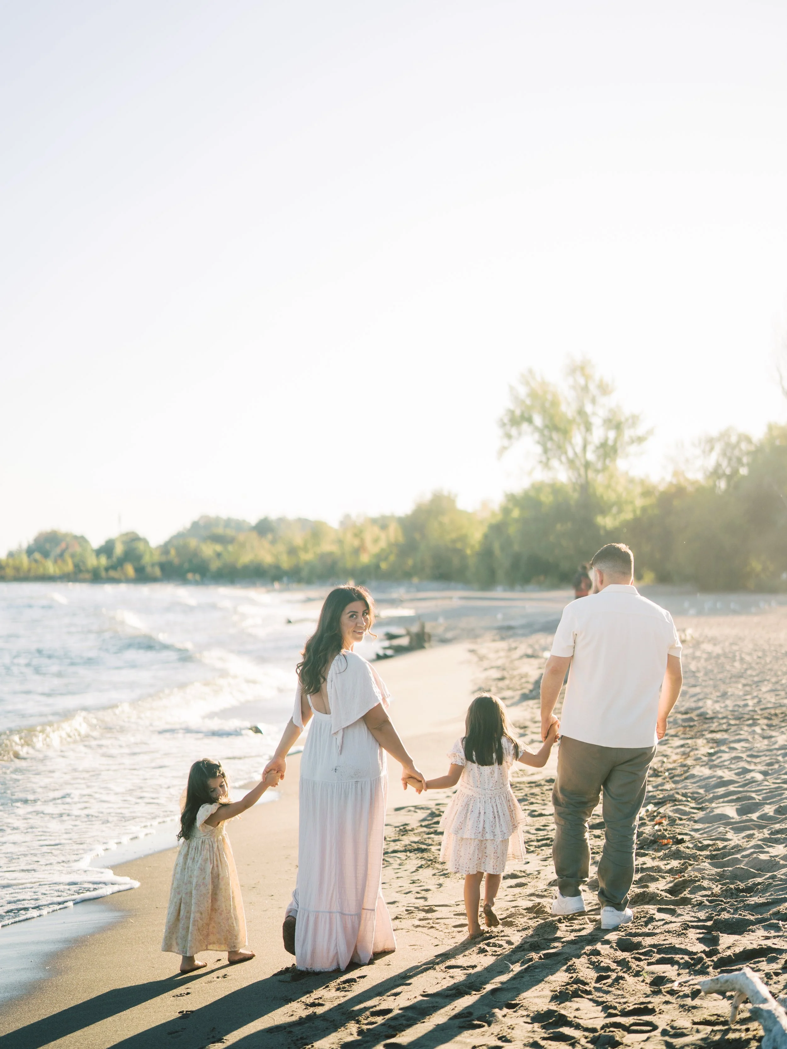 Family of four walking hand in hand along the beach during sunset.