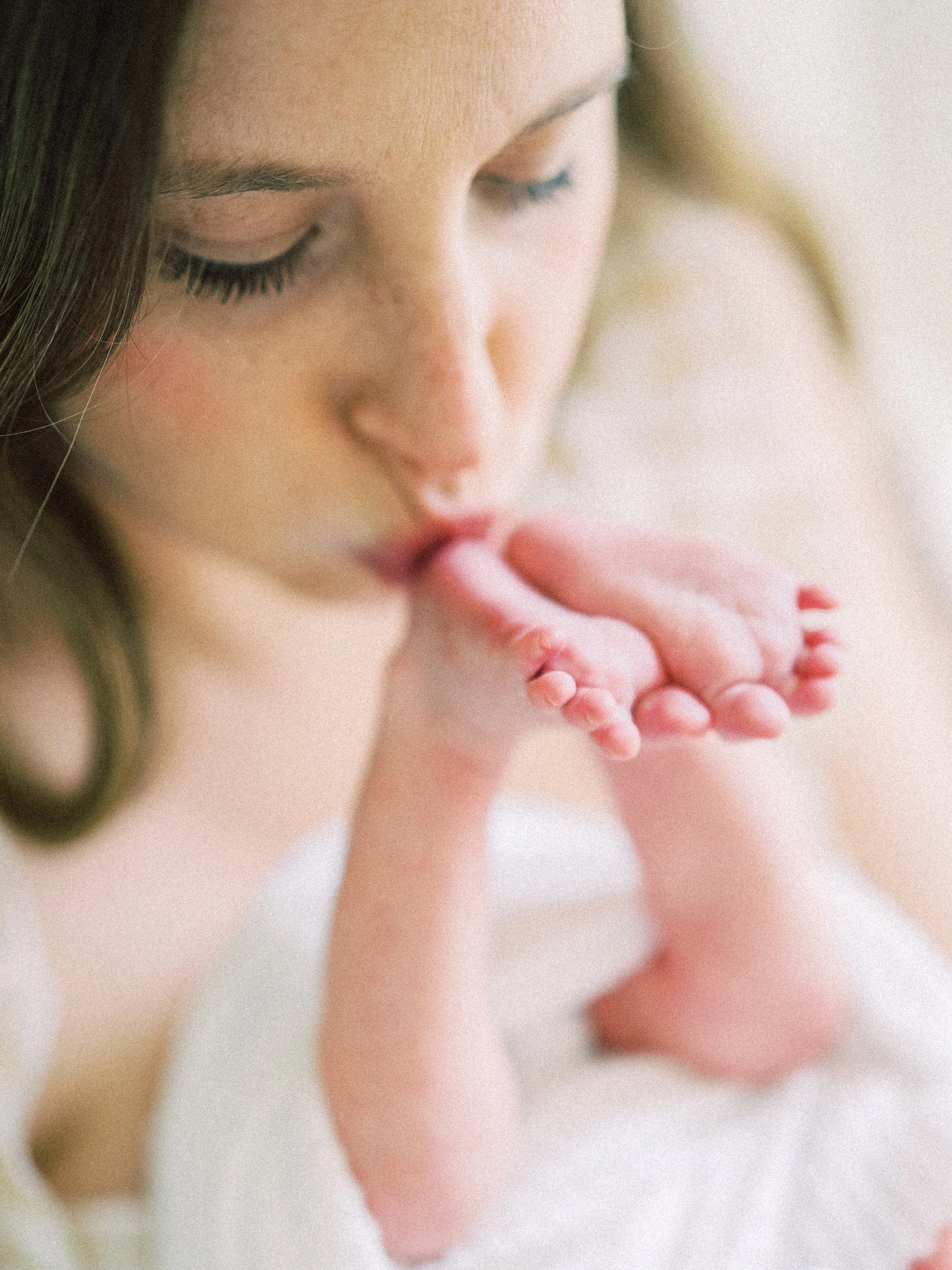 Close-up of a woman holding a newborn baby's hand near her lips.