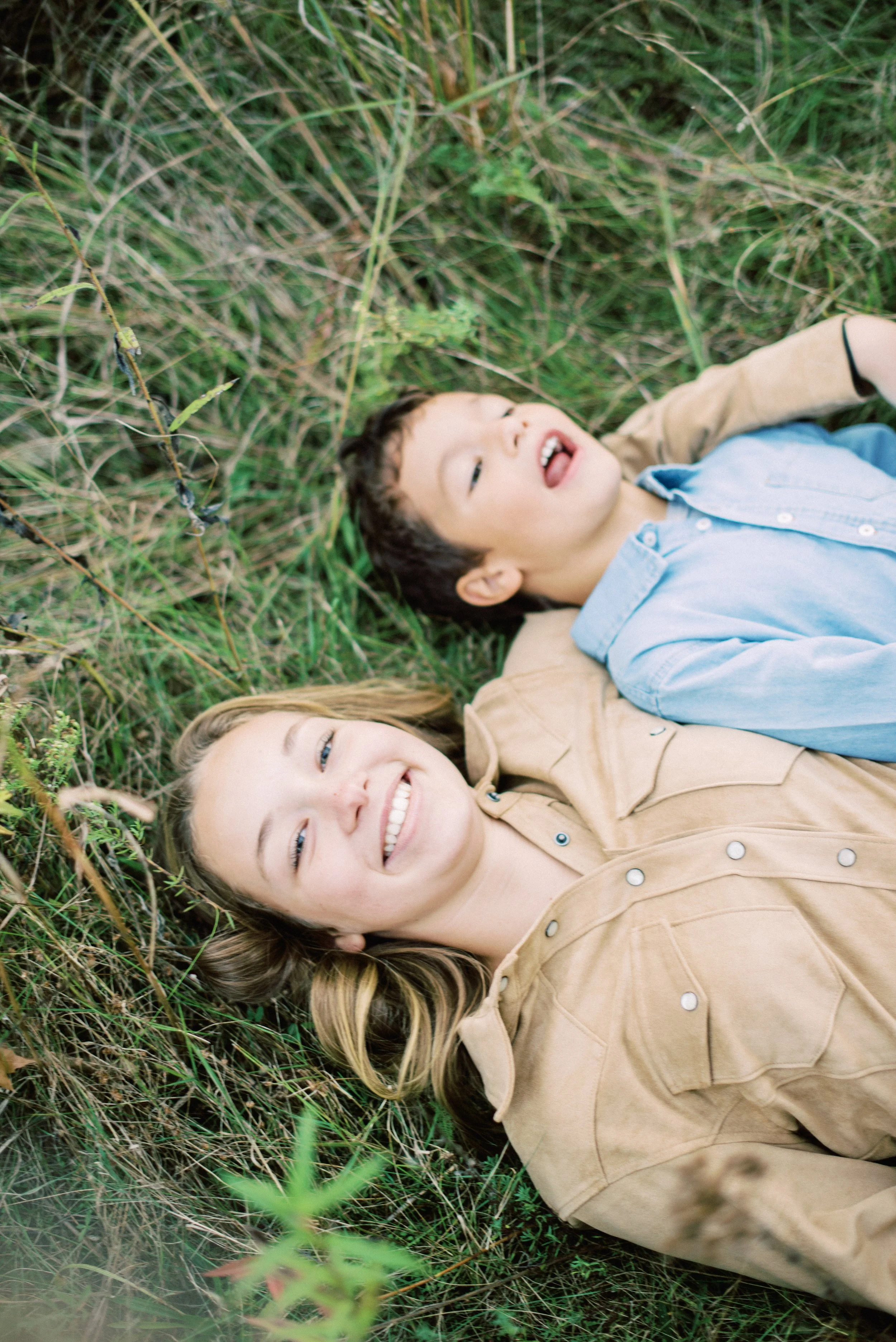 A woman and a young boy lying on grass among plants, smiling and looking up.