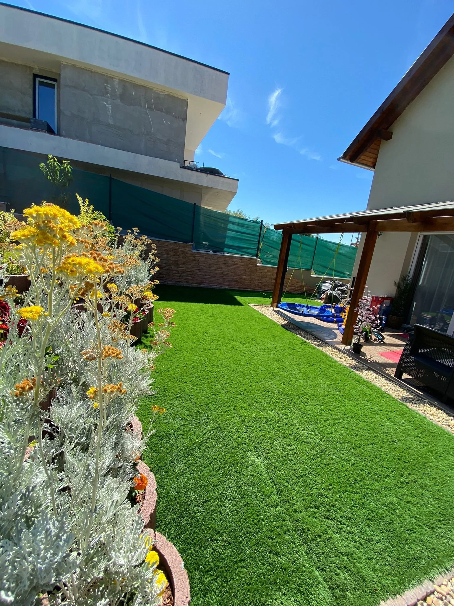 Garten mit grünem Rasen, Blumenbeet, moderne Gebäude im Hintergrund und blauer Himmel.