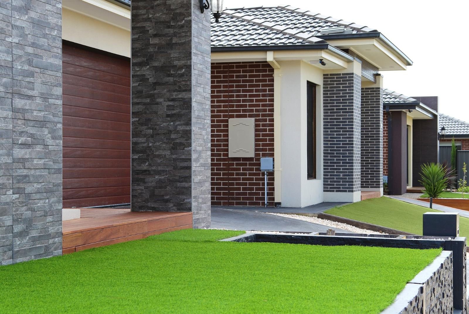 Moderner Hauseingang mit gemauerten Säulen, grünem Rasen und Ziegelwand.