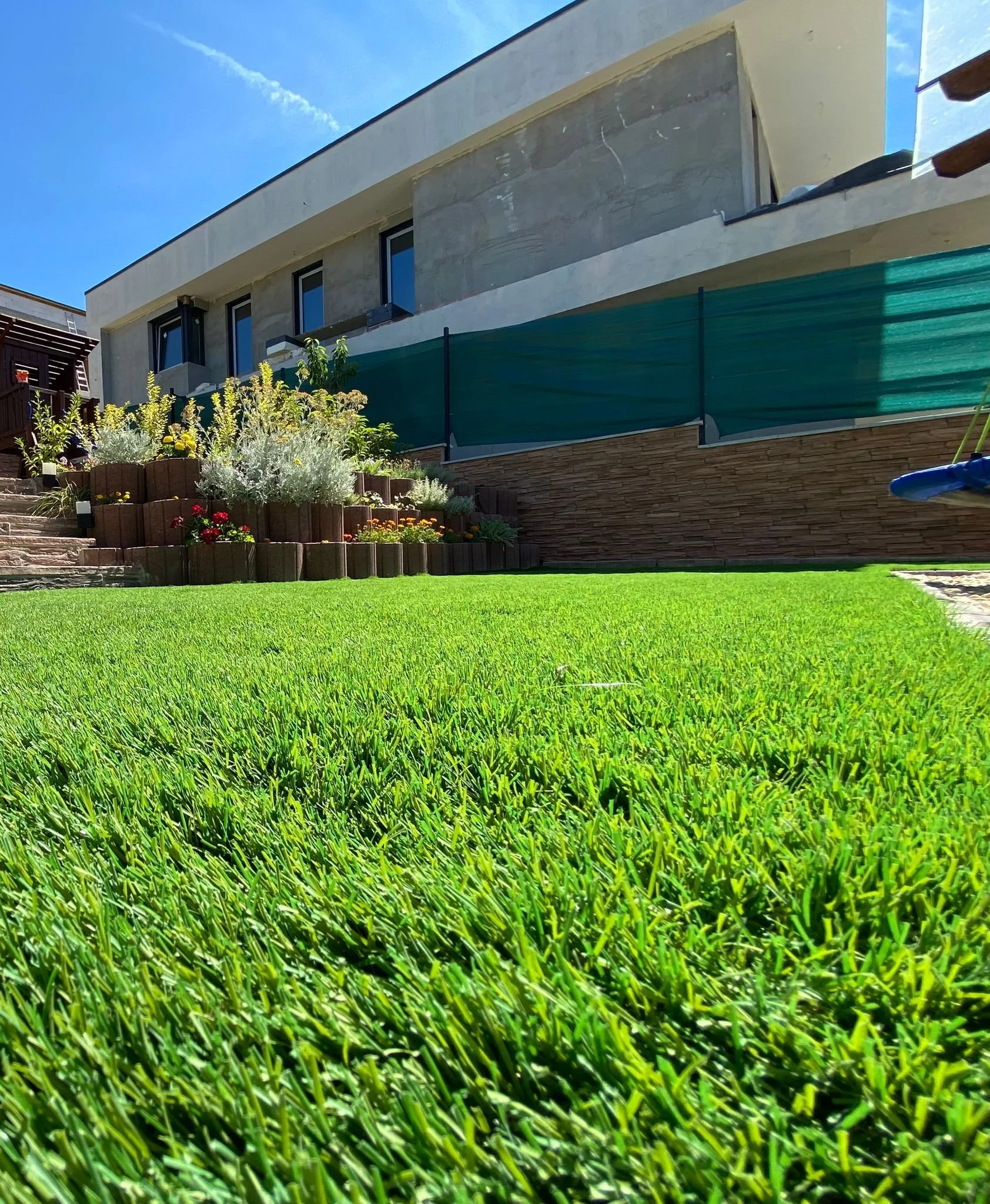 Moderner Garten mit gepflegtem Rasen, Blumenbeeten und einem modernen Gebäude im Hintergrund.