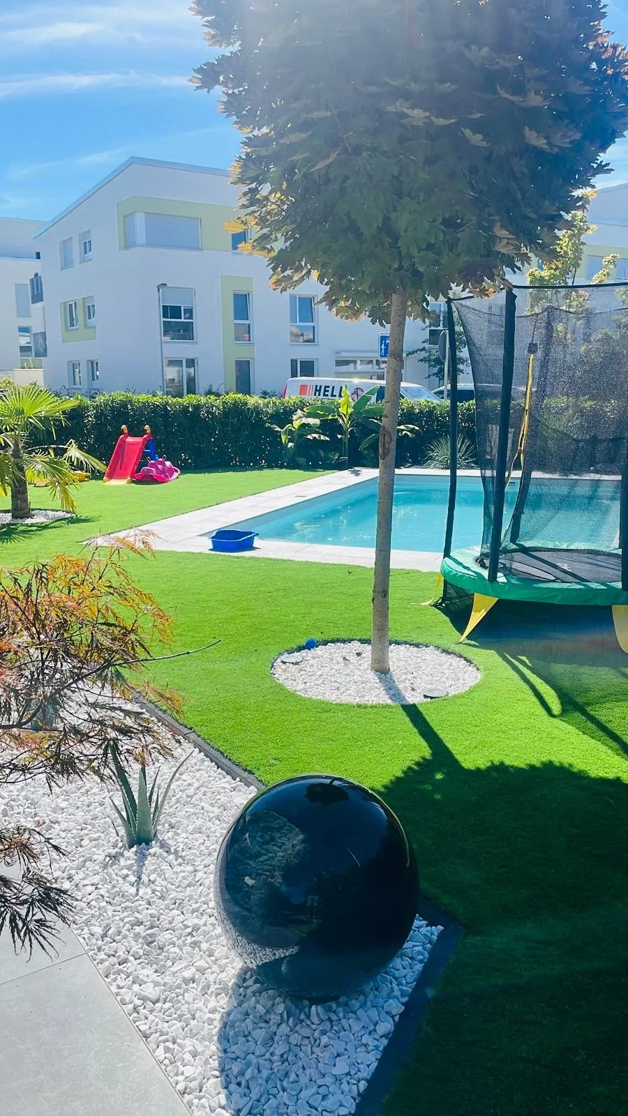 Moderner Garten mit Trampolin, Rutsche, Swimmingpool, Steinen und Pflanzen.