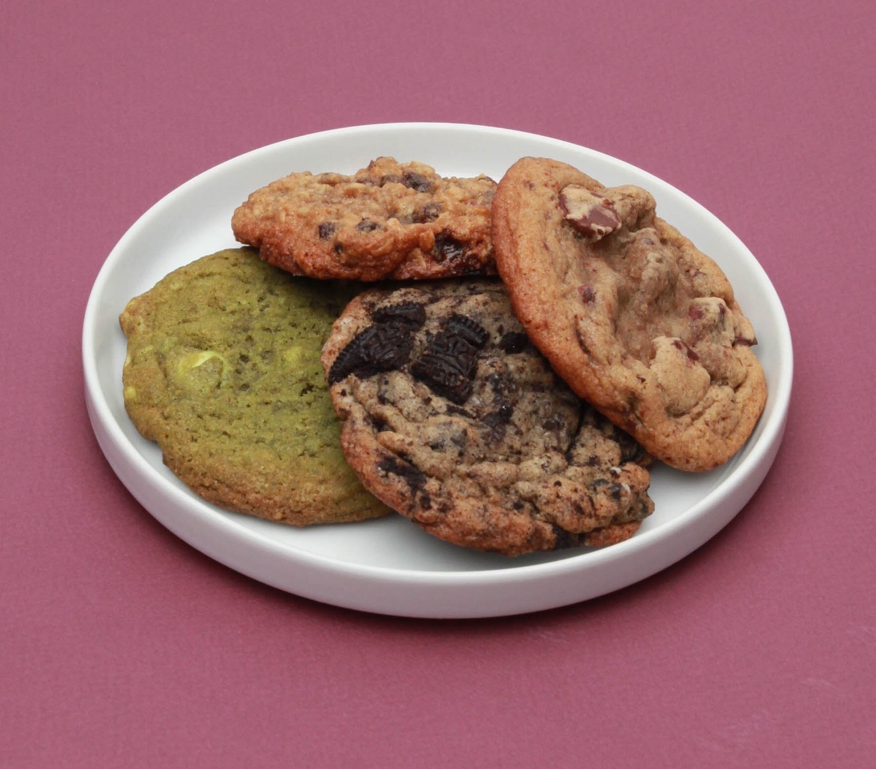 Assorted cookies on a white plate against a pink background.