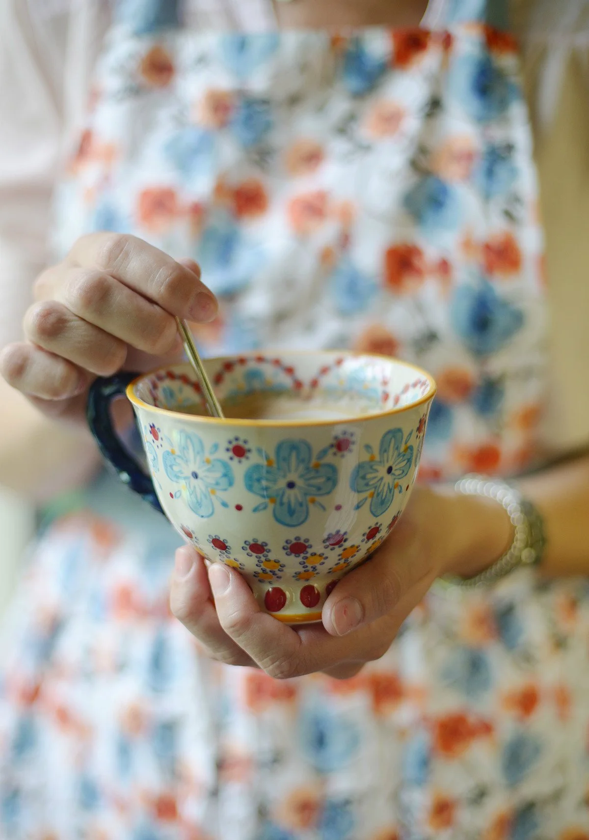 A person in a floral apron holding a colorful ceramic bowl with a spoon