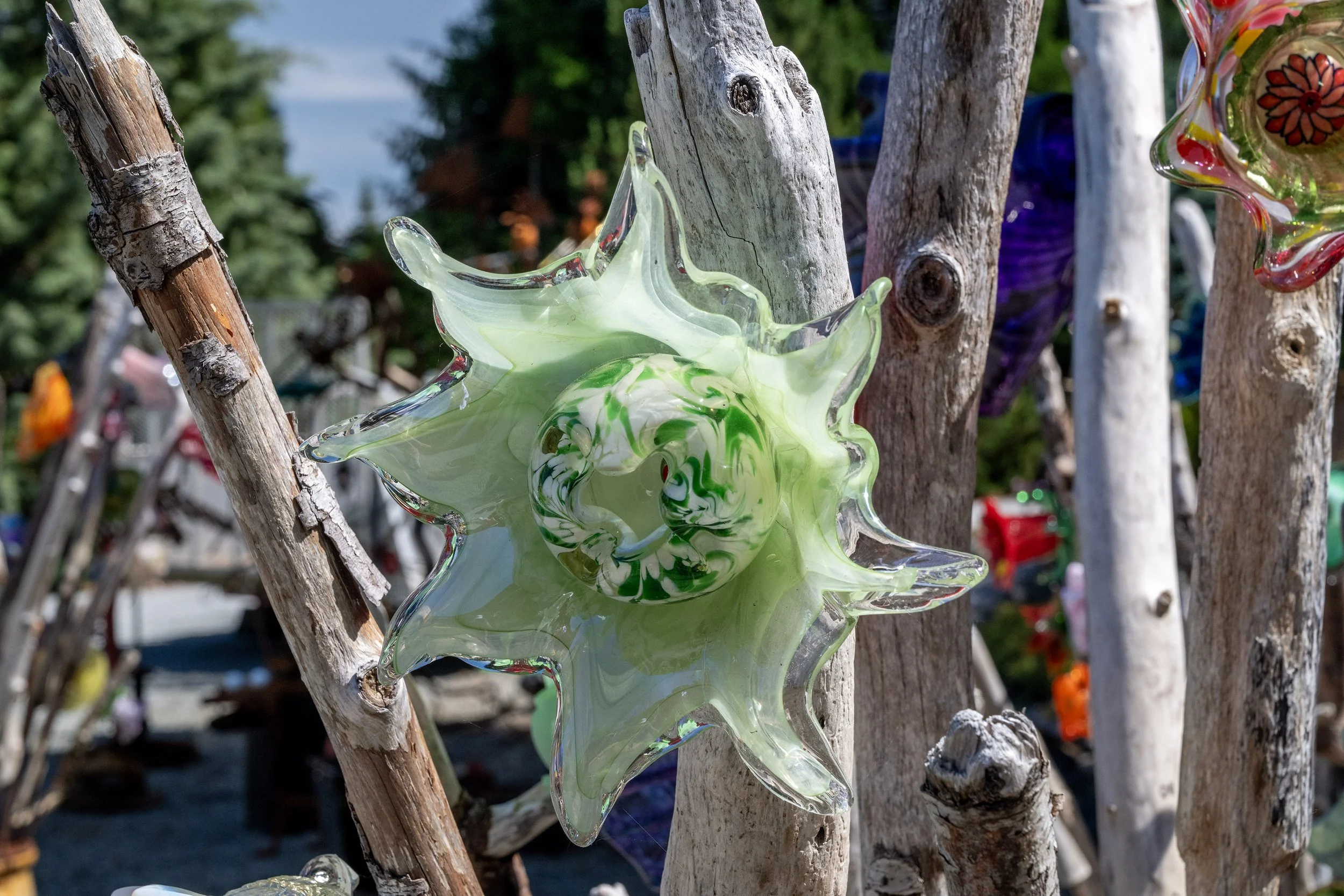 Colorful glass art piece resembling a star or flower shape hanging on a wooden stick with other similar art pieces in the background.