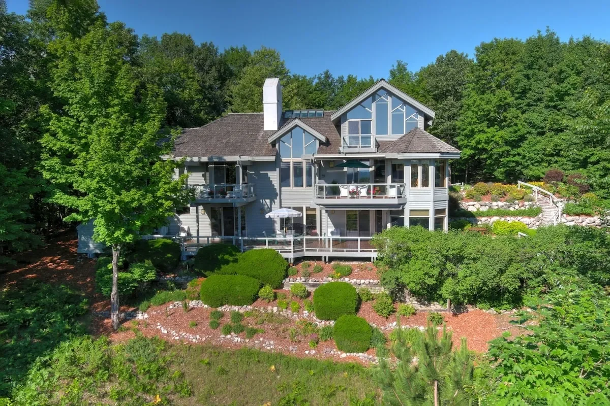 Sunset over a forested lake with silhouettes of trees and distant mountains.