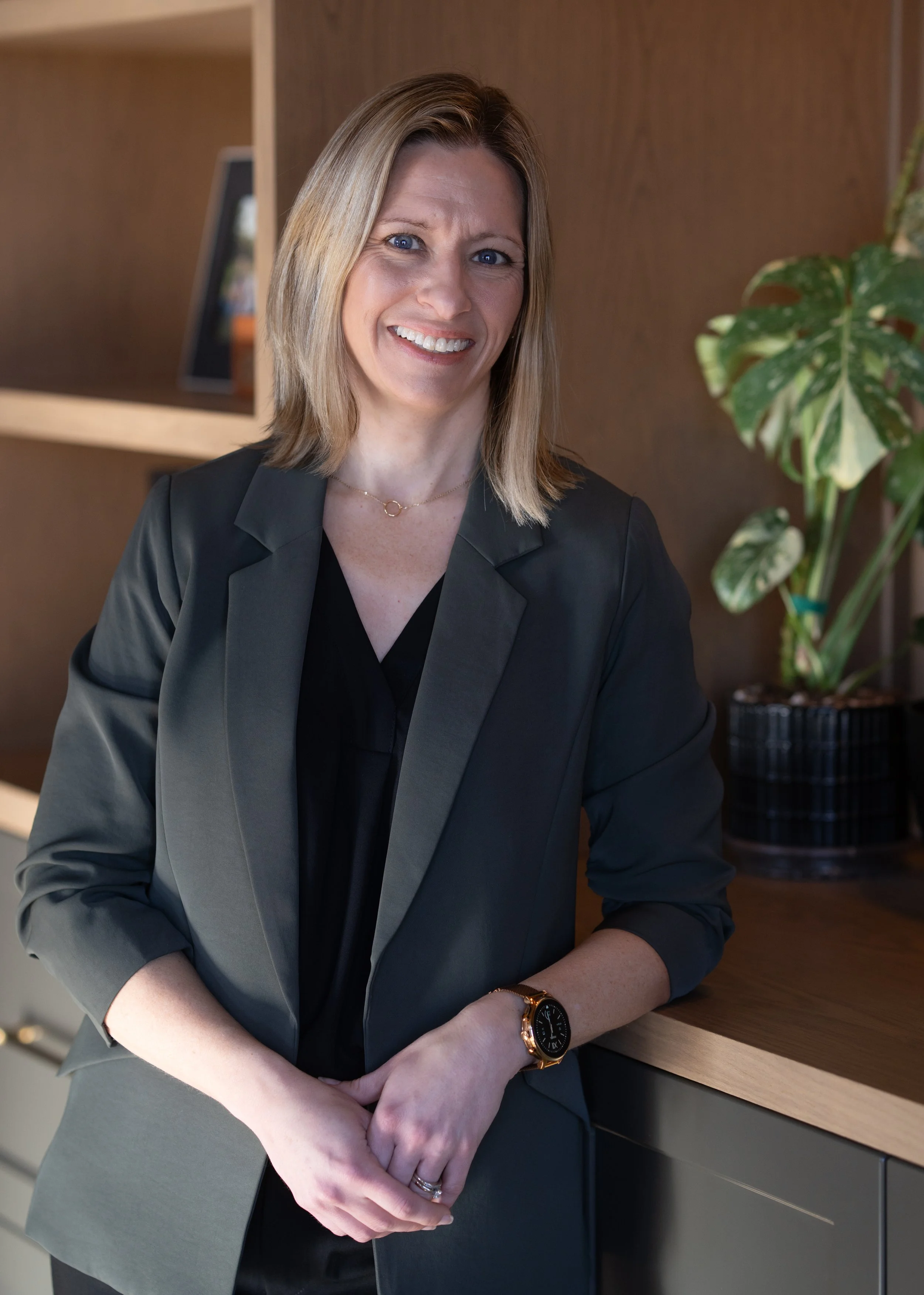 Portrait of a woman with blonde hair wearing a blue top and black cardigan against a gray background.