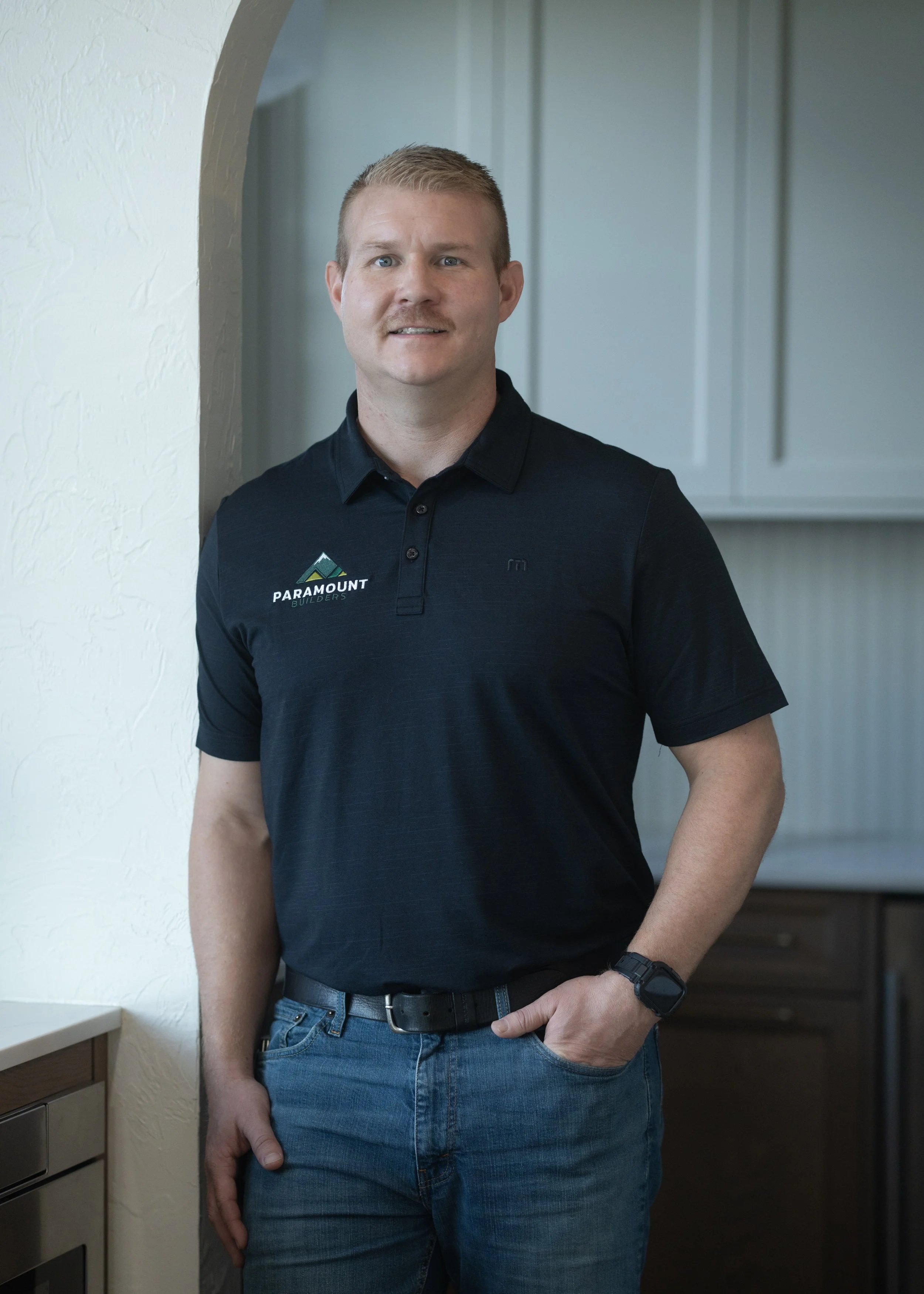 Portrait of a man in a collared shirt with a logo, set against a gray background.