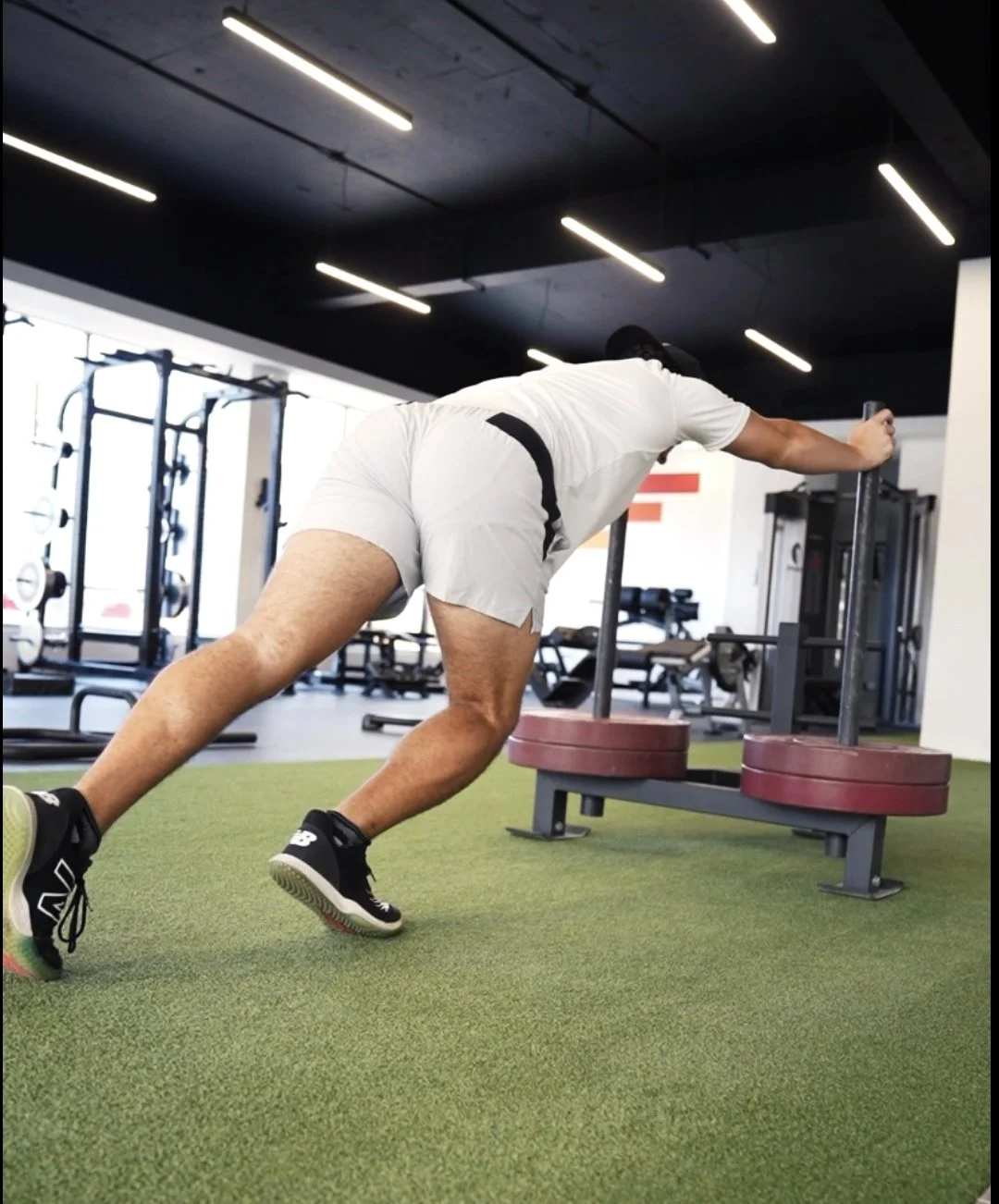 A man pushing a heavy sled with weights in a gym. He is leaning forward with his arms extended, engaging in a strength training exercise.