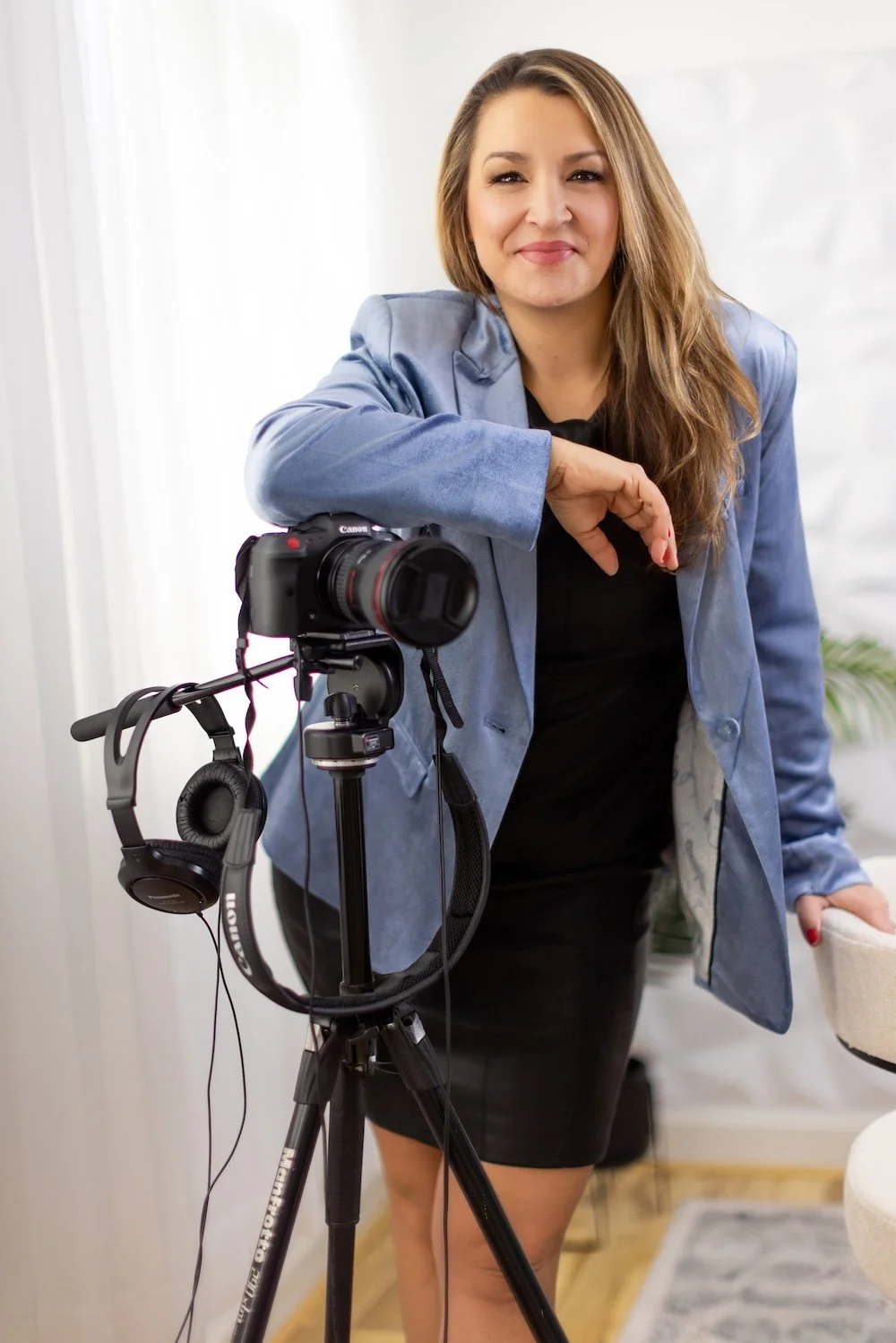 A professional studio portrait of Caryn Grafton, smiling and leaning on a camera