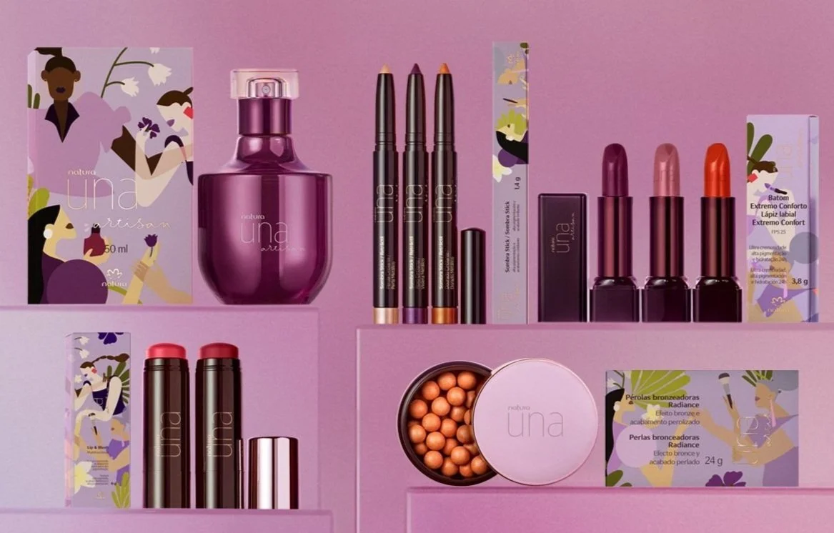 Natura Una cosmetic products on pink background, including perfume, lipsticks, makeup pencils, and packaging.