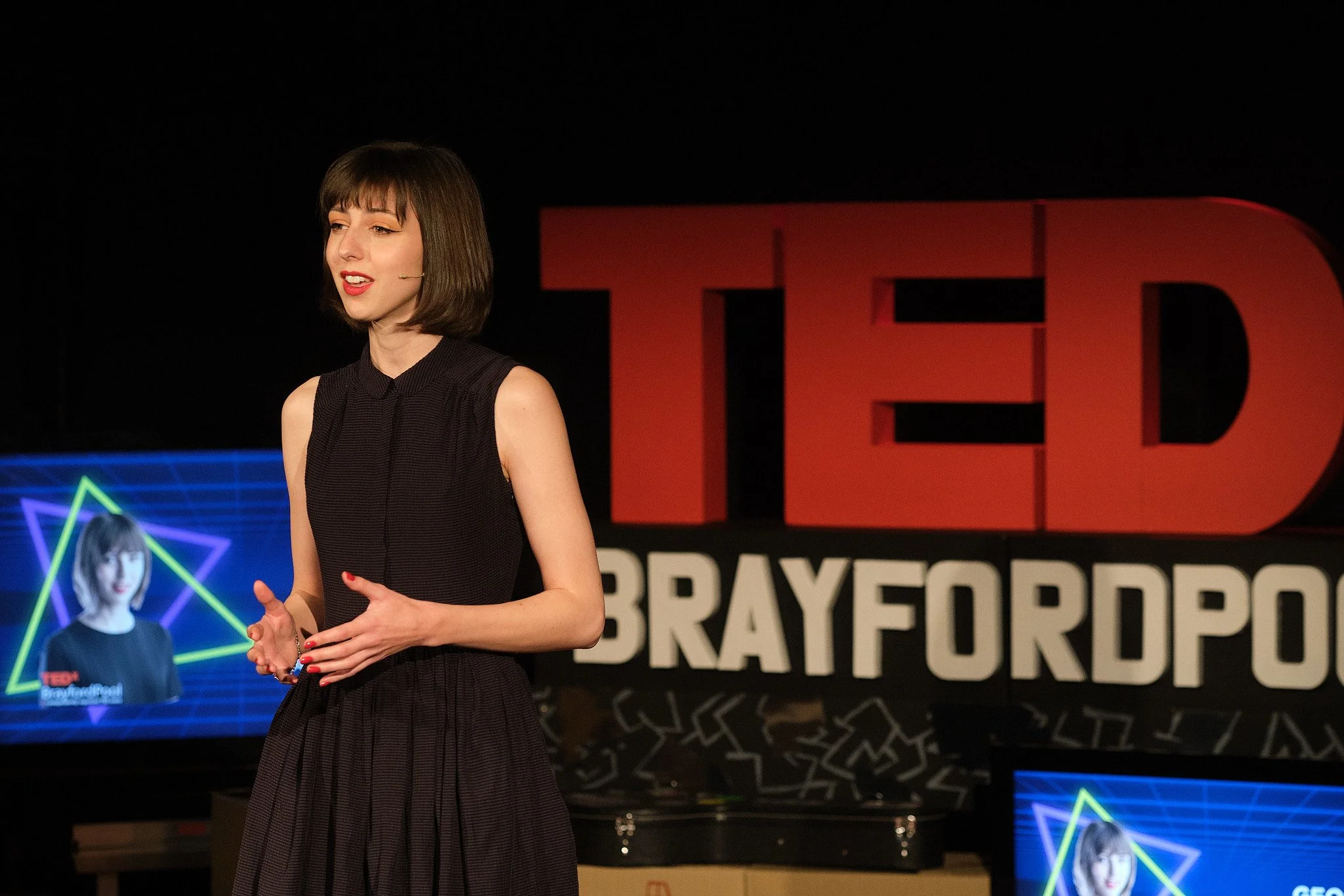Georgia Preece on stage at TEDx Brayford Pool. She is performing spoken word poetry to an audience.
