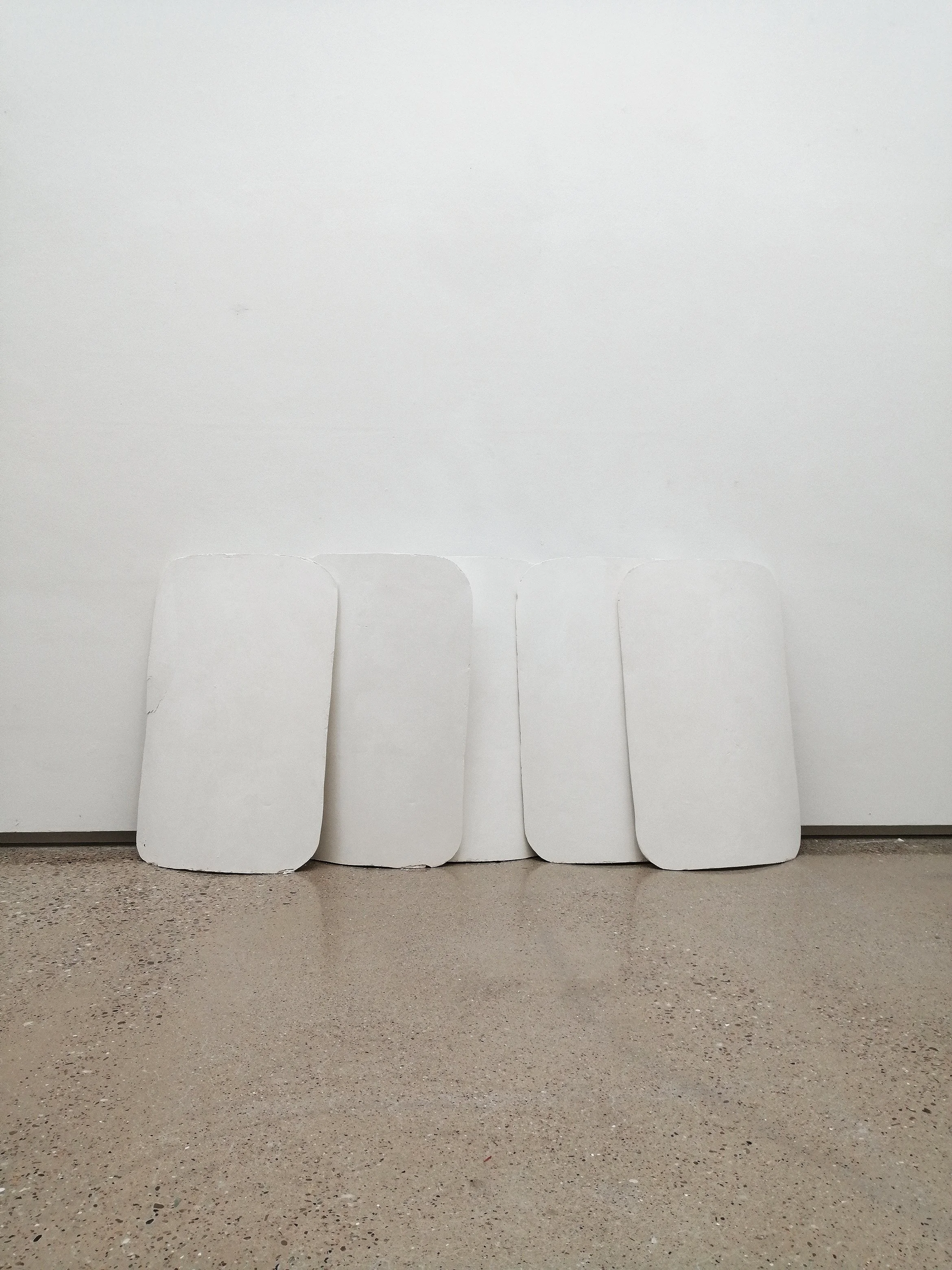 Four white representations of a police riot shields made from plaster displayed in a gallery space.