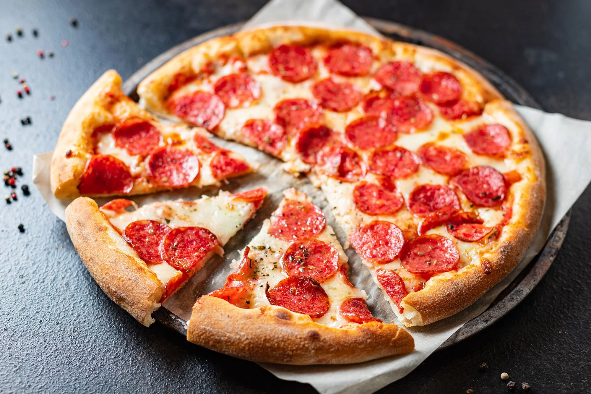 A pepperoni pizza with slices missing on a dark surface.