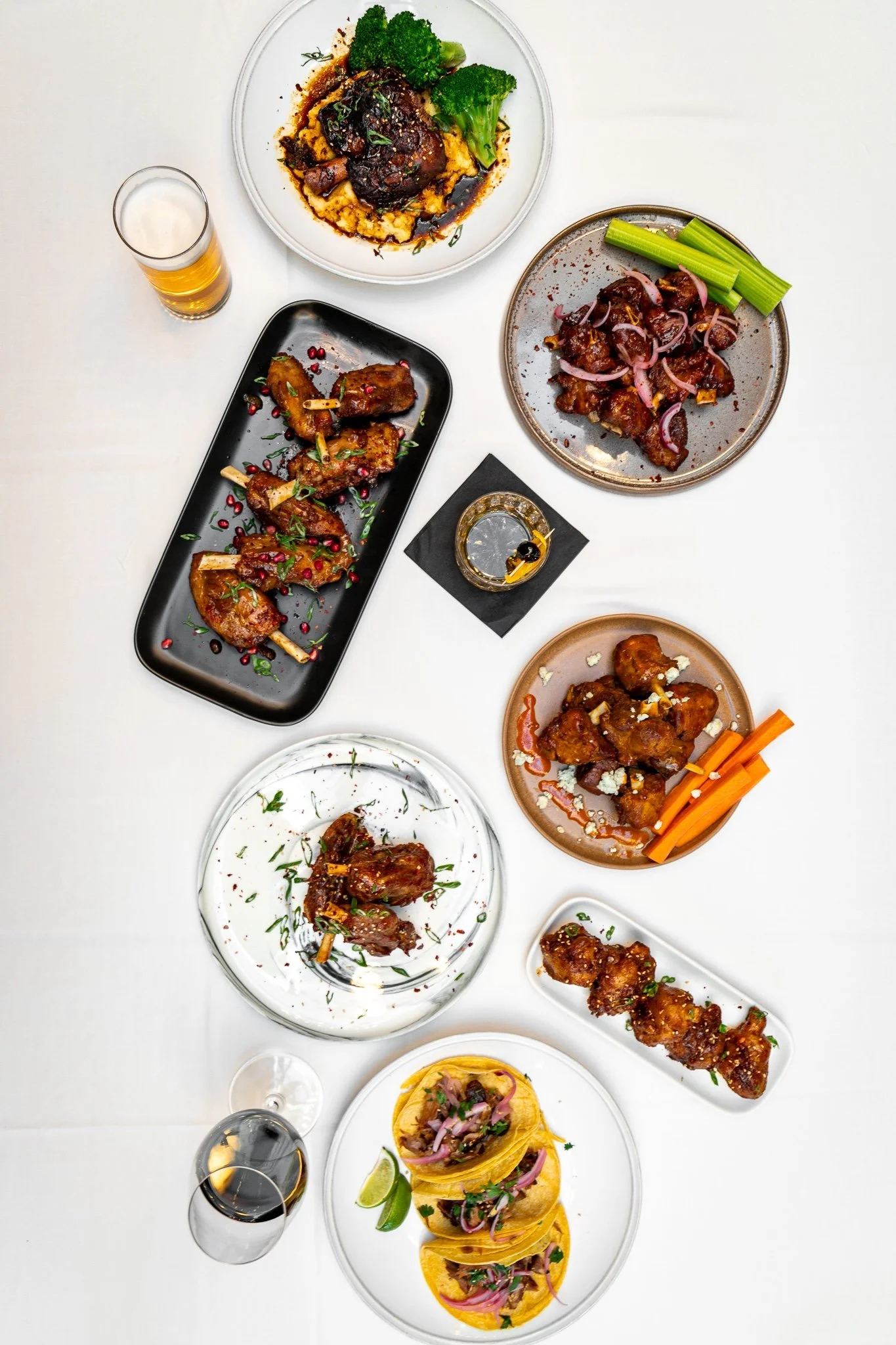 An overhead view of various plates of Pig Wings along with drinks on a white table.