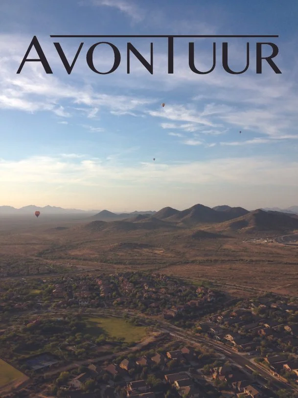 Aerial view of a suburban area with houses, greenery, and mountain ranges in the background under a partly cloudy sky, with the word 'AVONTUUR' overlaid at the top.