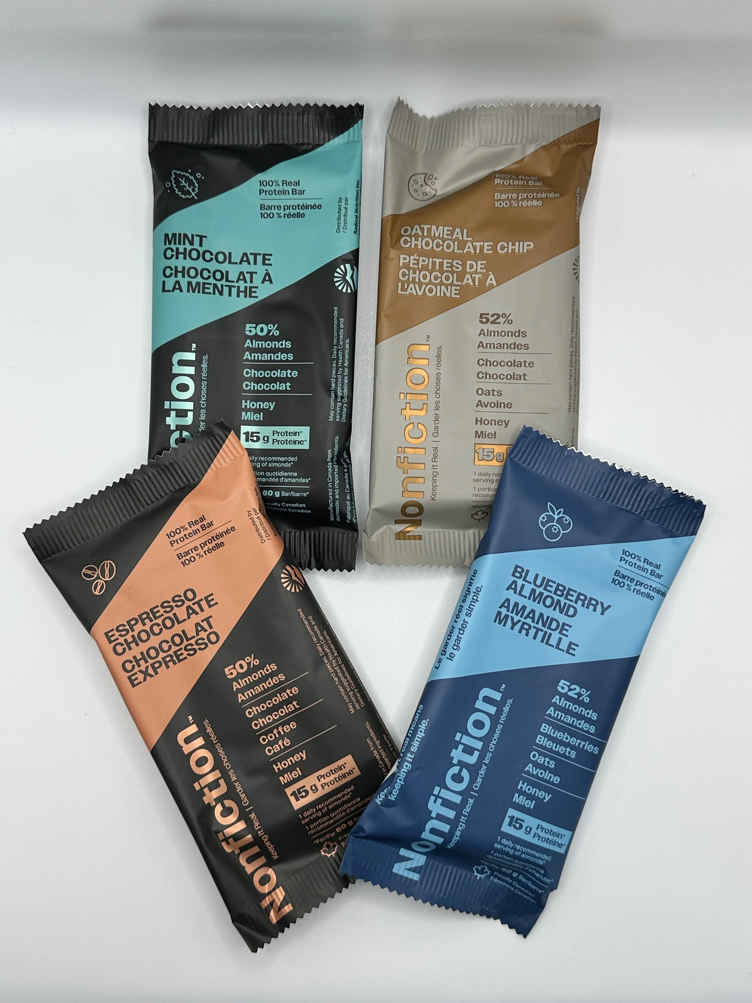 Four flavored protein bars: mint chocolate, oatmeal chocolate chip, espresso chocolate, and blueberry almond, arranged on a white surface.