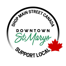 Circular logo with black and green text promoting downtown St. Marys in Canada, encouraging shopping and supporting local businesses, with a red maple leaf.