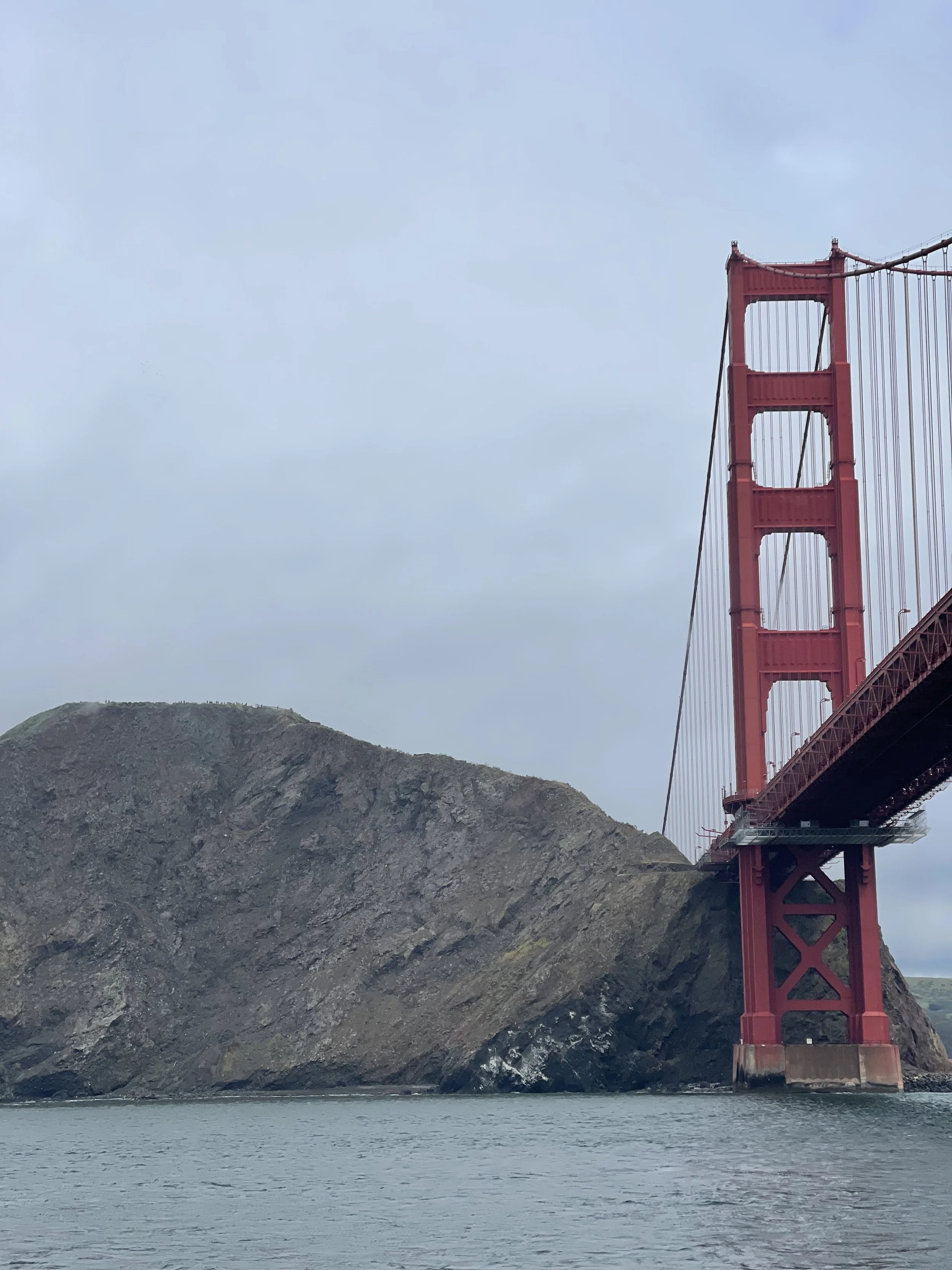 The Golden Gate Bridge in San Francisco, California, with a view of one of its towers and a hilly landscape in the background during cloudy weather.