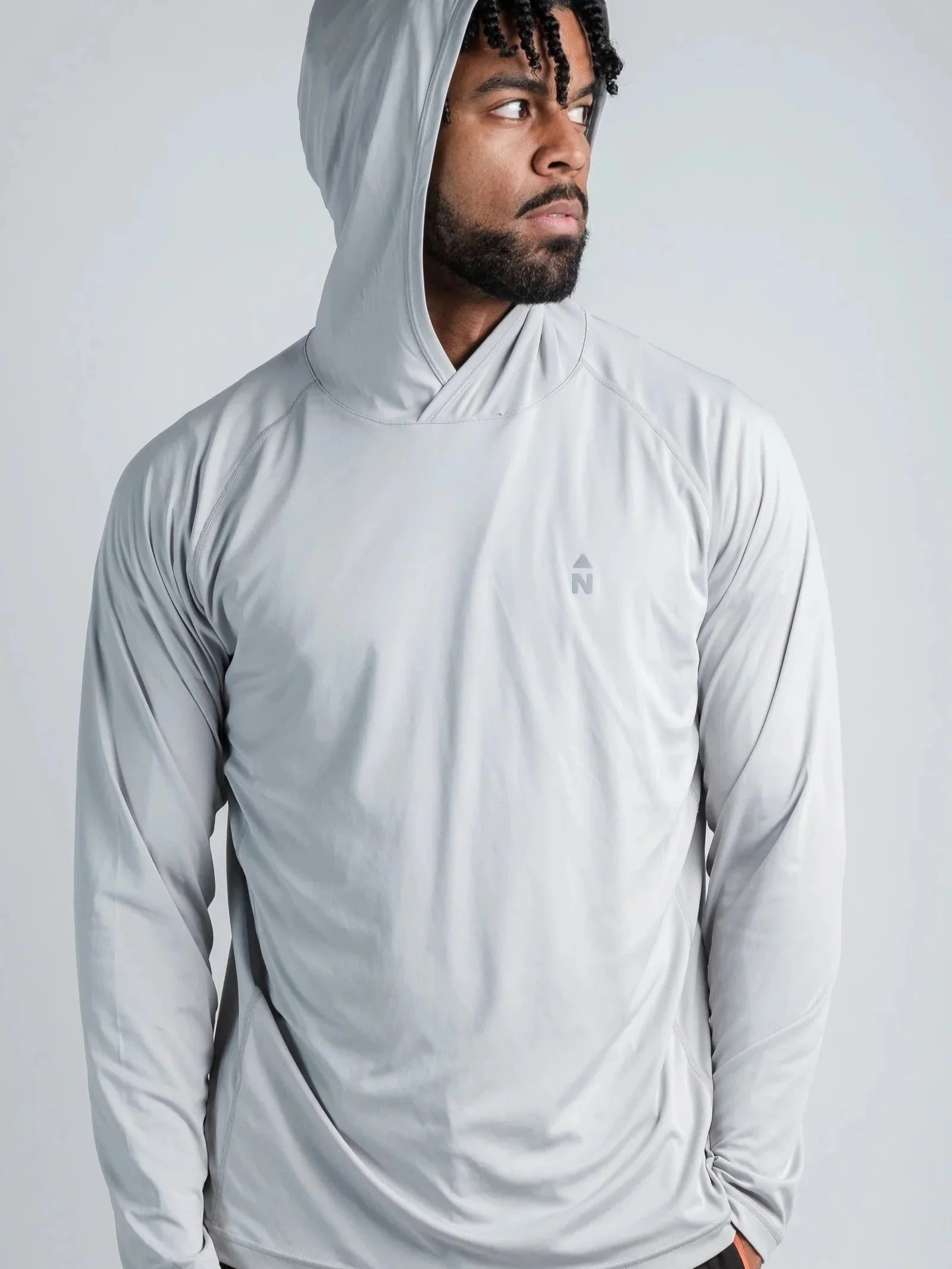 A man wearing a light gray hooded athletic shirt with the hood up, looking to the right against a plain light gray background.