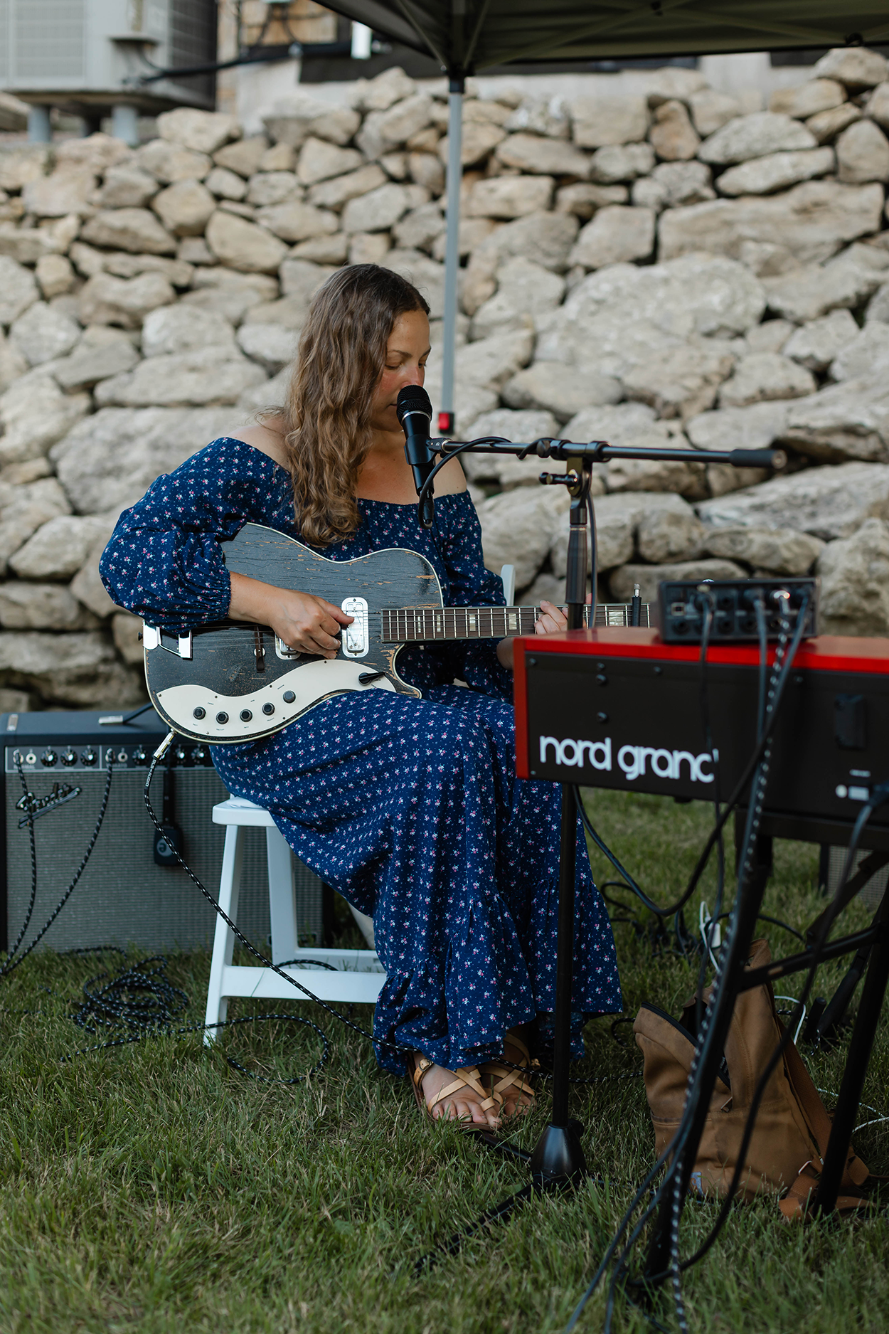 A singer in a blue dress singing with a stone wall background.