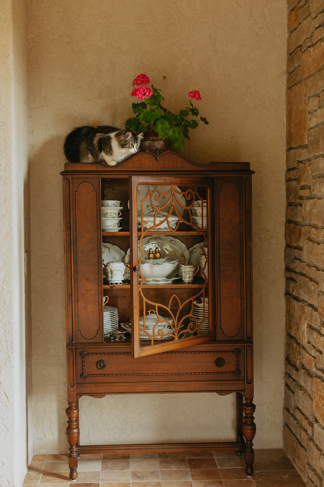 Vintage wooden china hutch filled with china and a cat sitting atop of it.