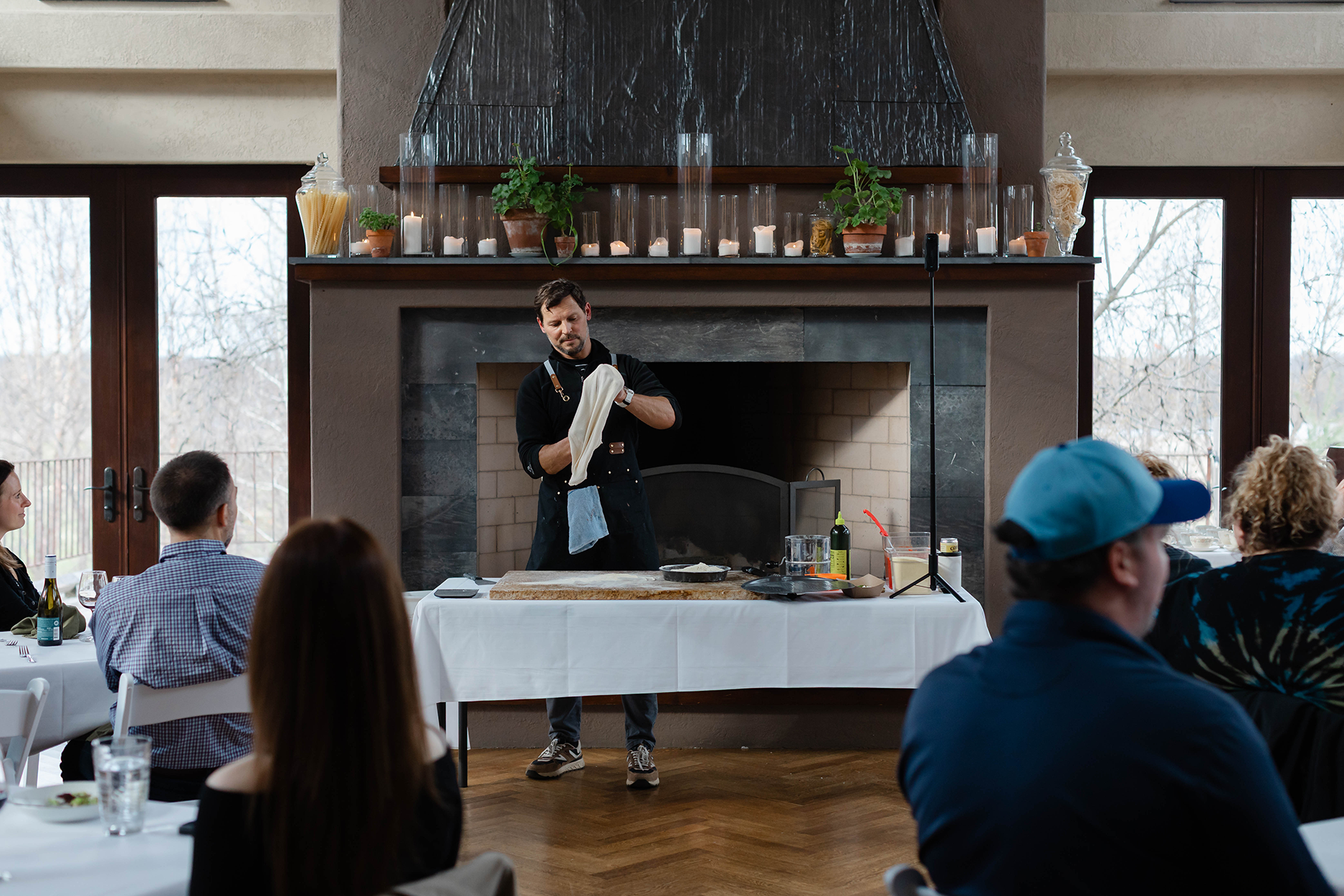 Instructor standing in front of a fireplace teaching how to make pizza.