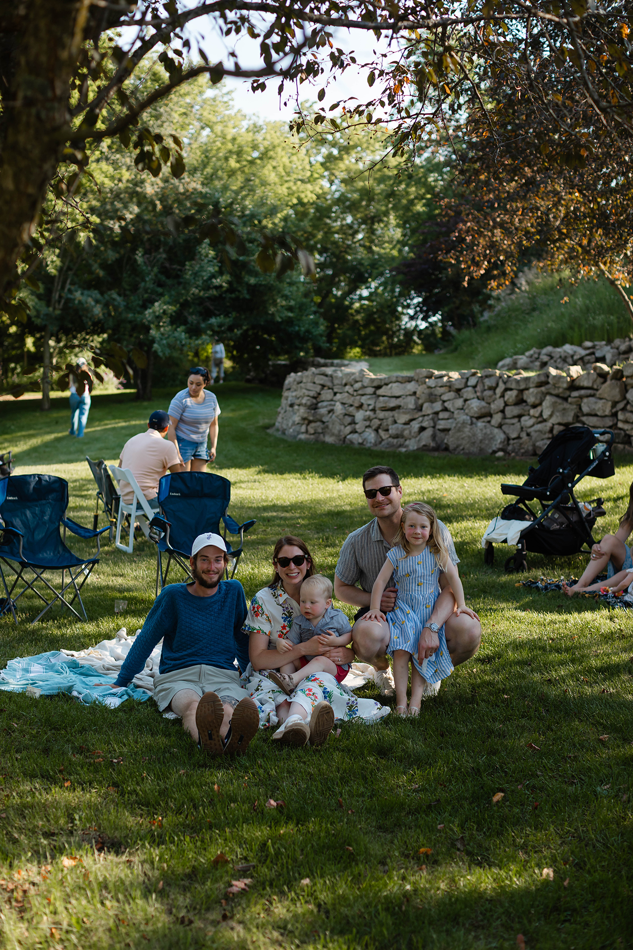 A group posing for a photo on top of a picnic blanket in the middle of an orchard.