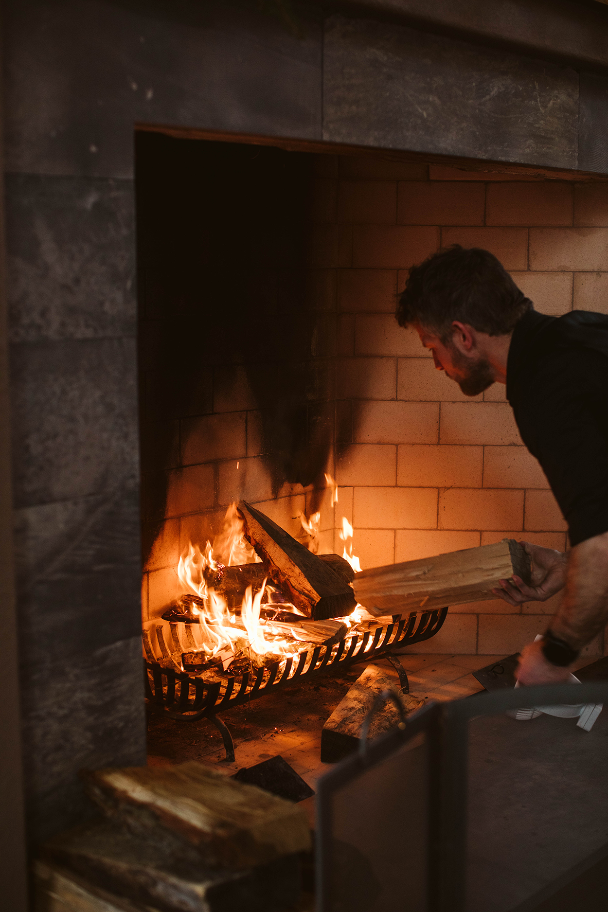A man stoking the fire of a large fireplace.