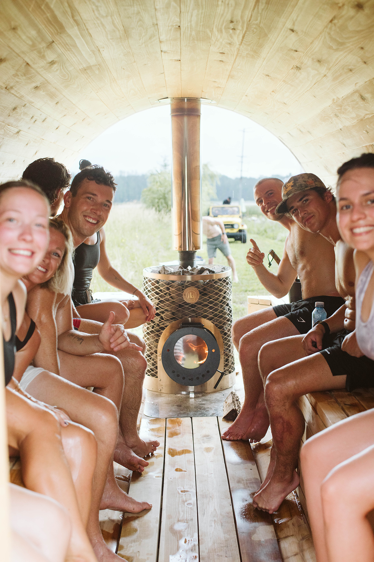 A group of people enjoying a wood fire sauna with a large window in the background.