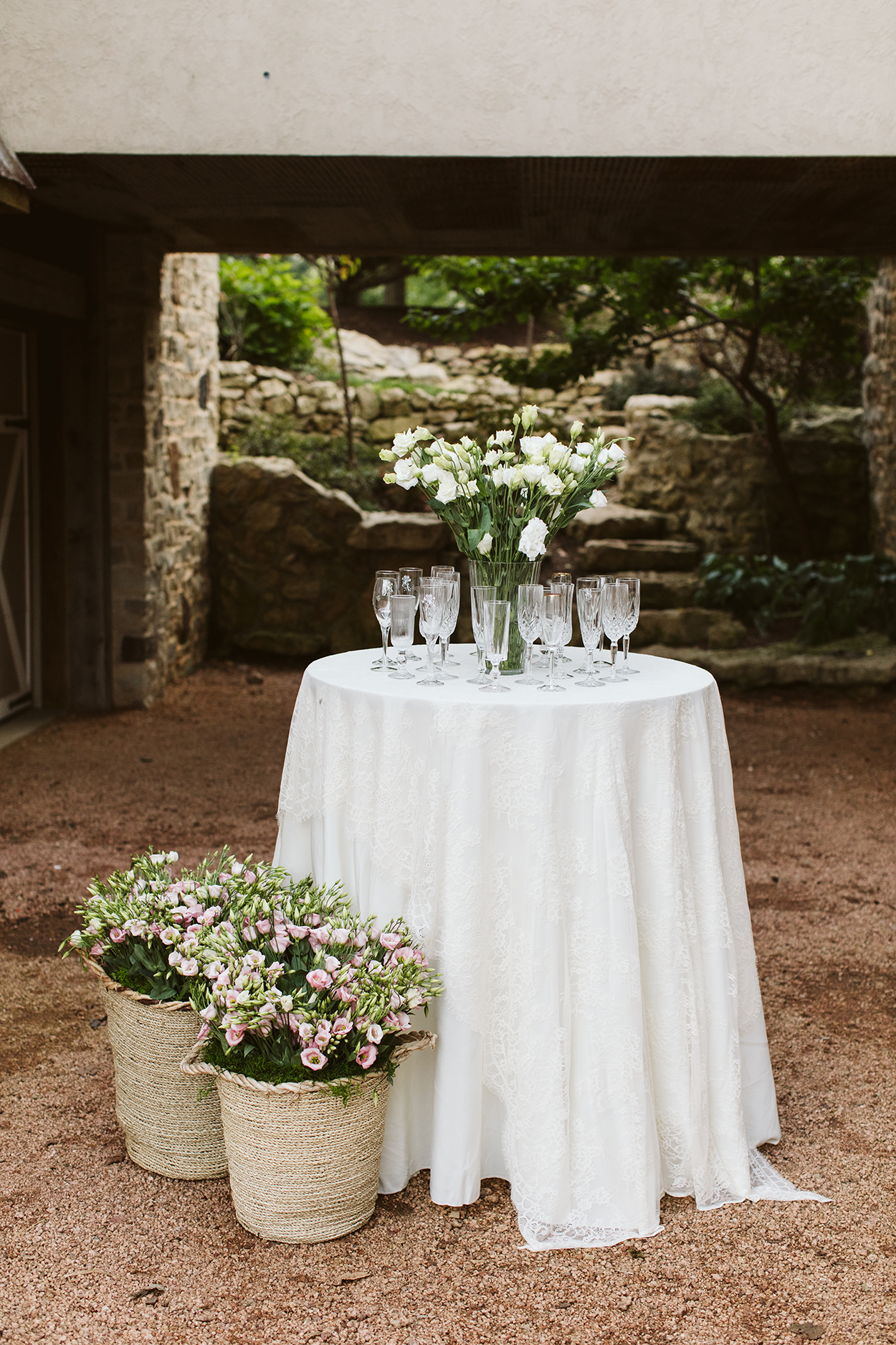 Wedding champagne toast table surrounded by floral baskets set in front of a beautiful manicured stone walled garden.