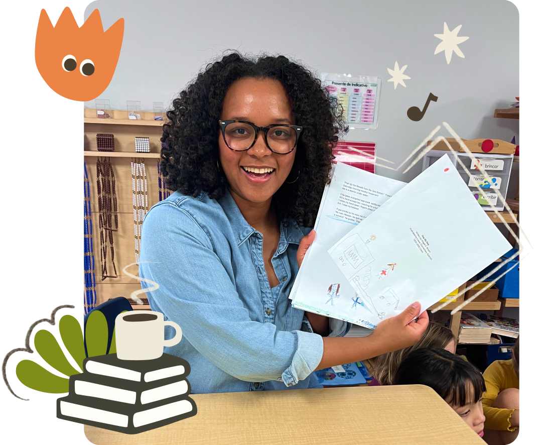 A smiling woman with curly black hair and glasses holding up children's drawings in a classroom setting, with other kids at a desk and classroom decorations in the background.