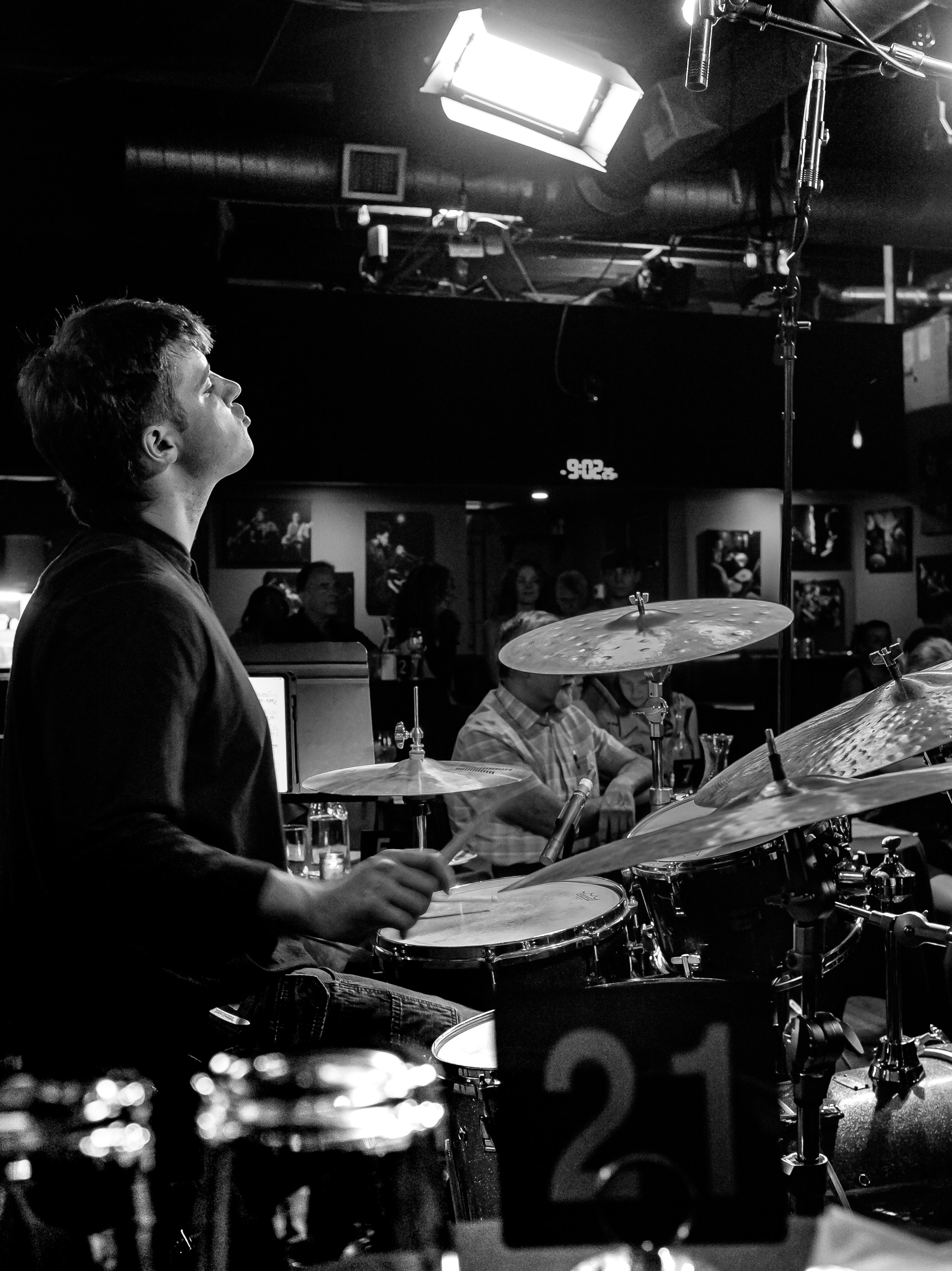 Black and white photo from behind of a young man at a drum set.