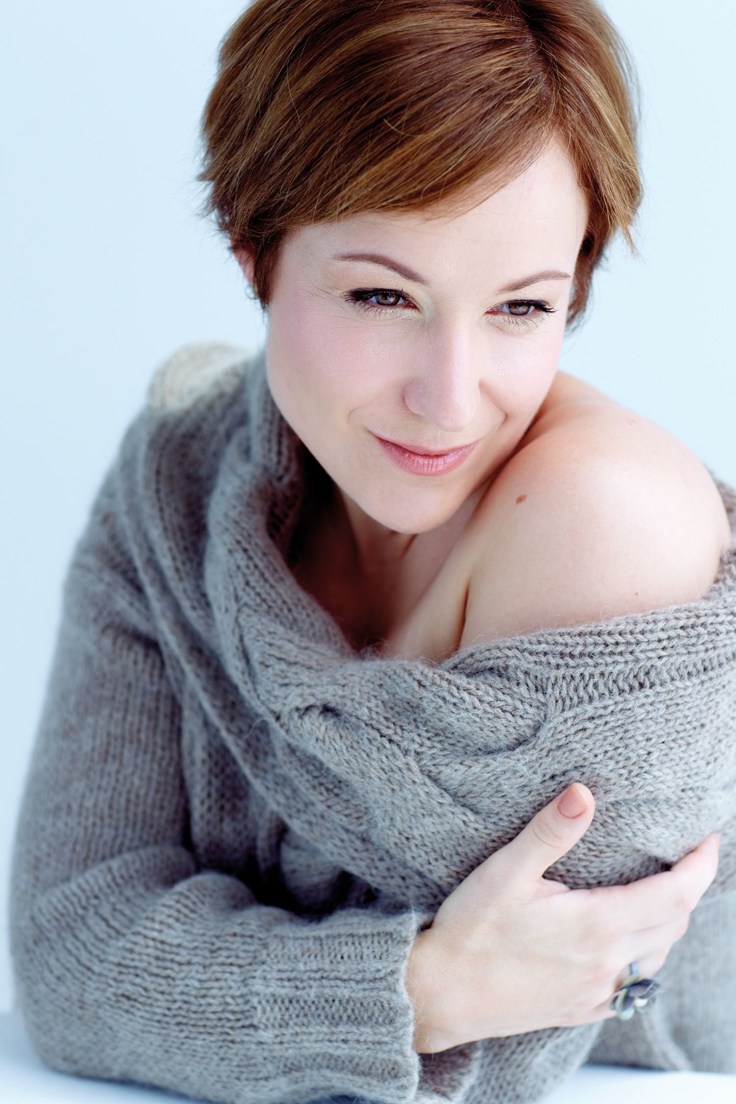 Woman gazing awkwardly down and off across her bare sweater draped shoulder.
