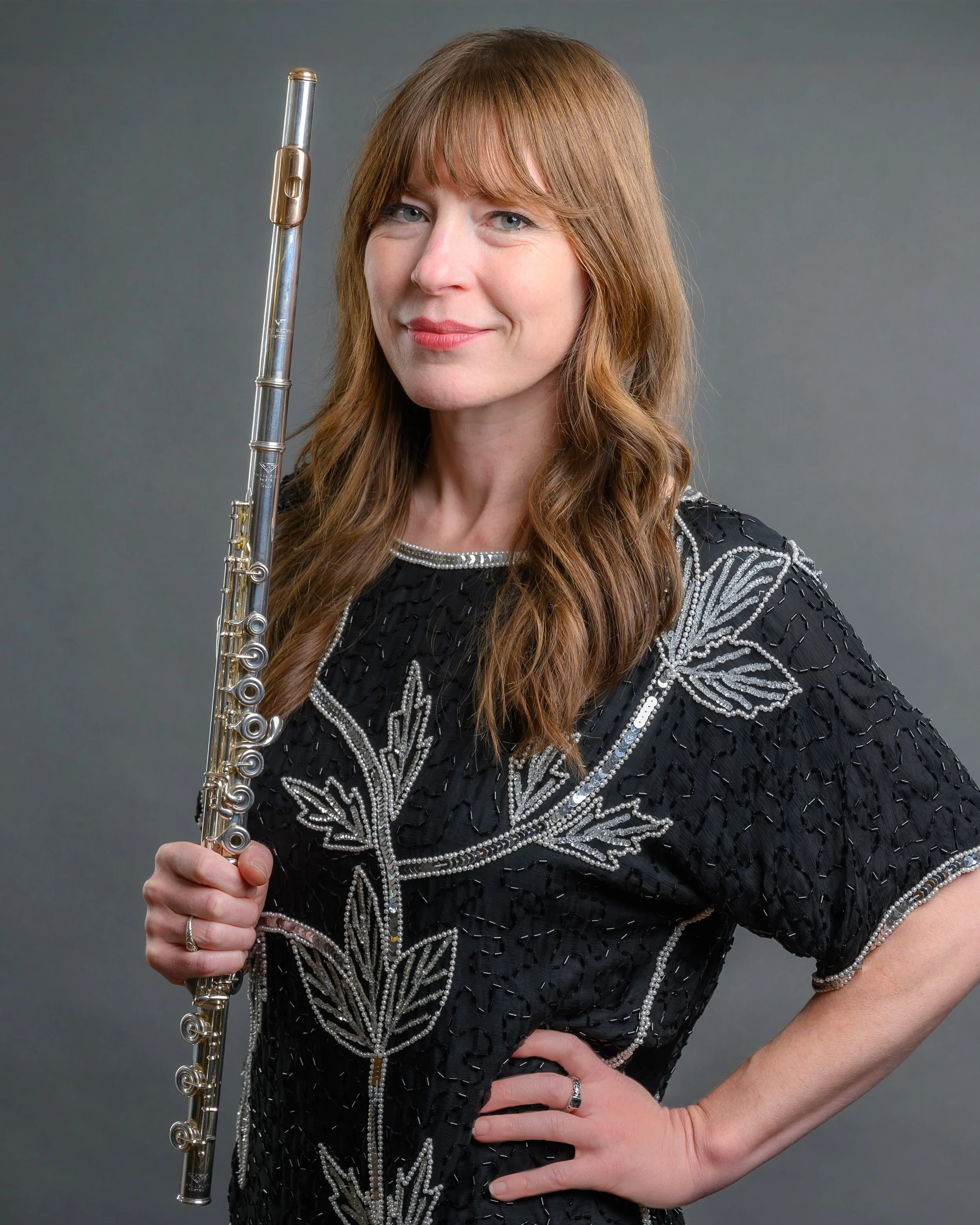 Smiling woman in a black beaded top posing with a flute