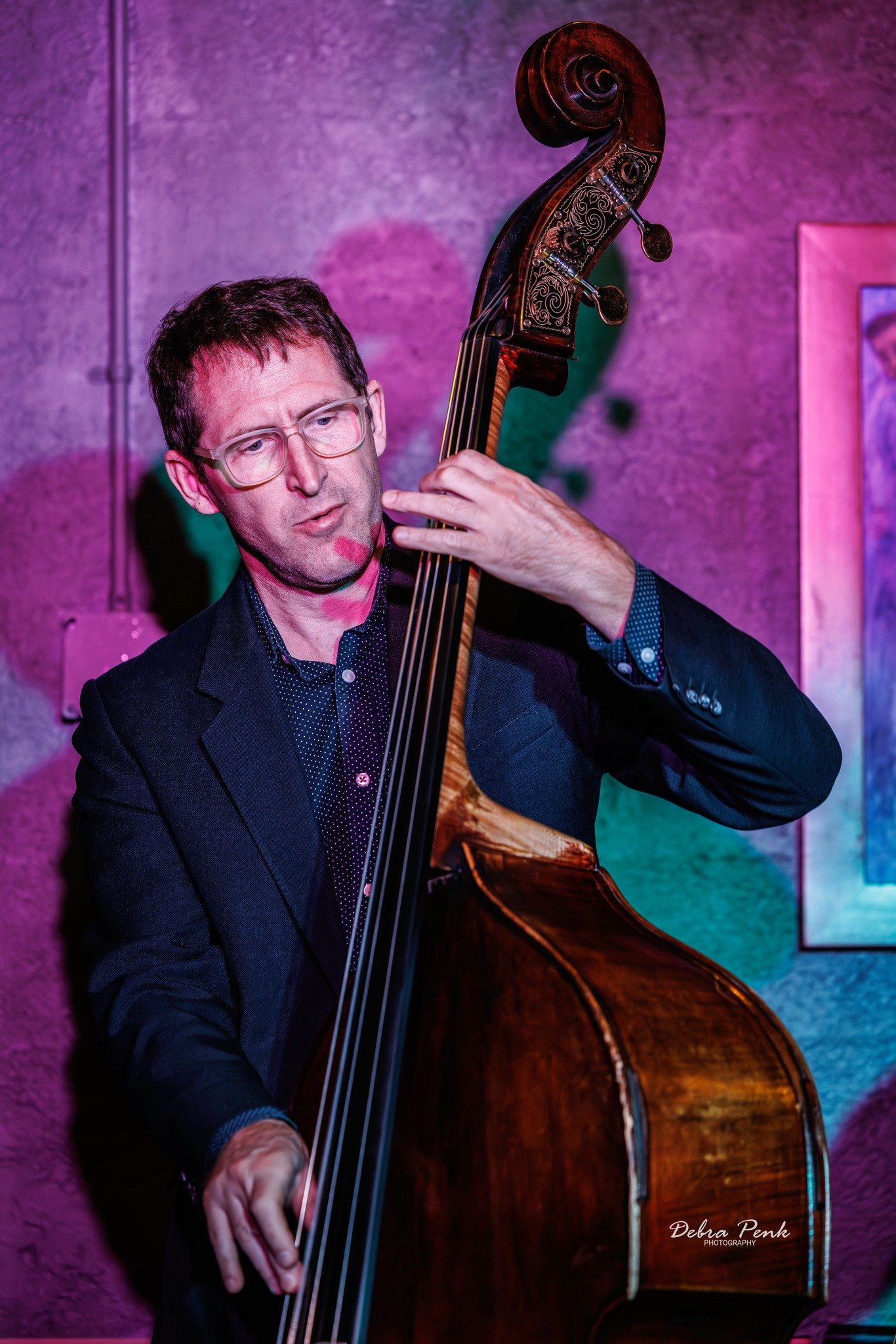 Man with glasses playing an upright base in a purple lit room