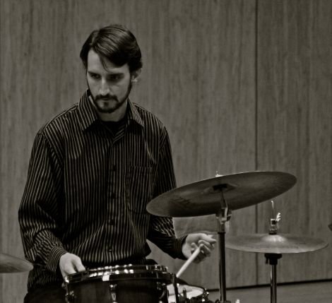 Black and white image of a man behind a drum set with an intense look on his face.