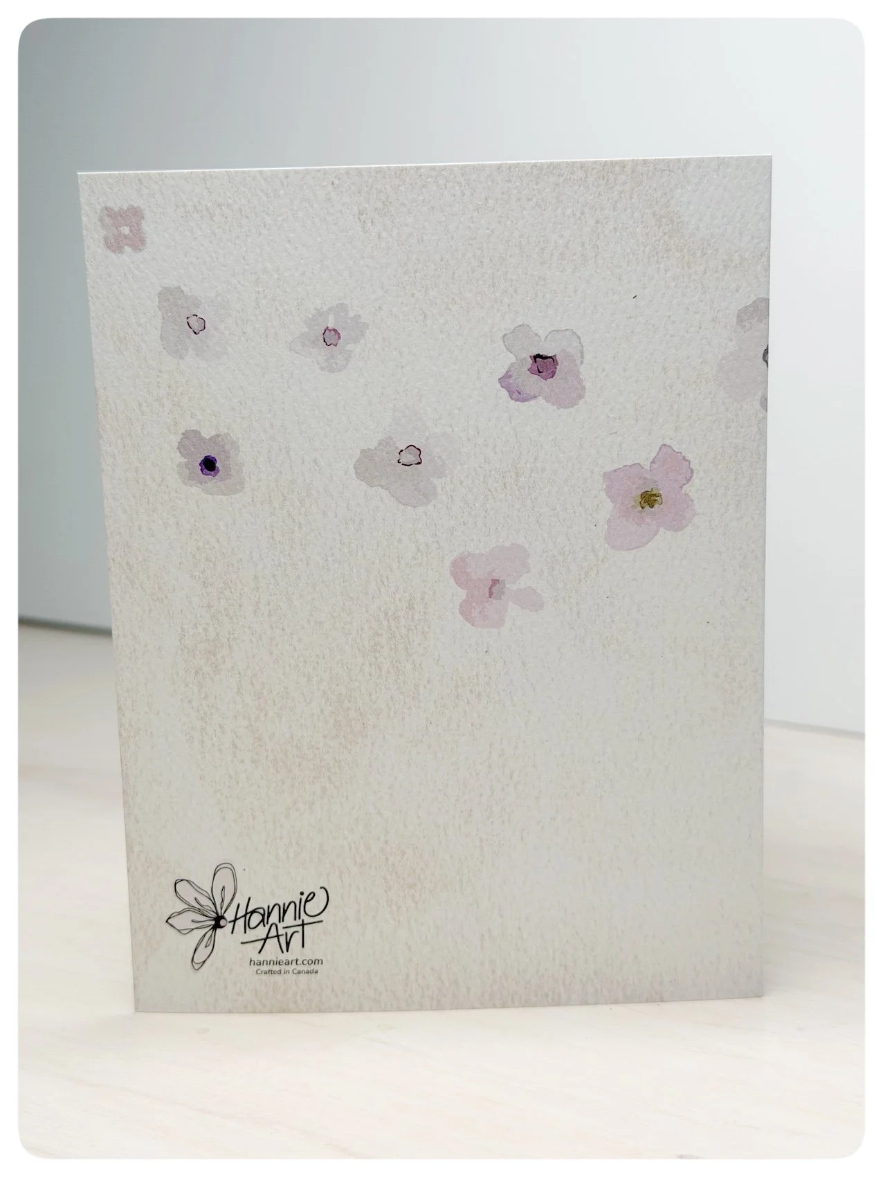 Back of baby girl pinafore greeting card with soft floral pattern and Hannie Art logo