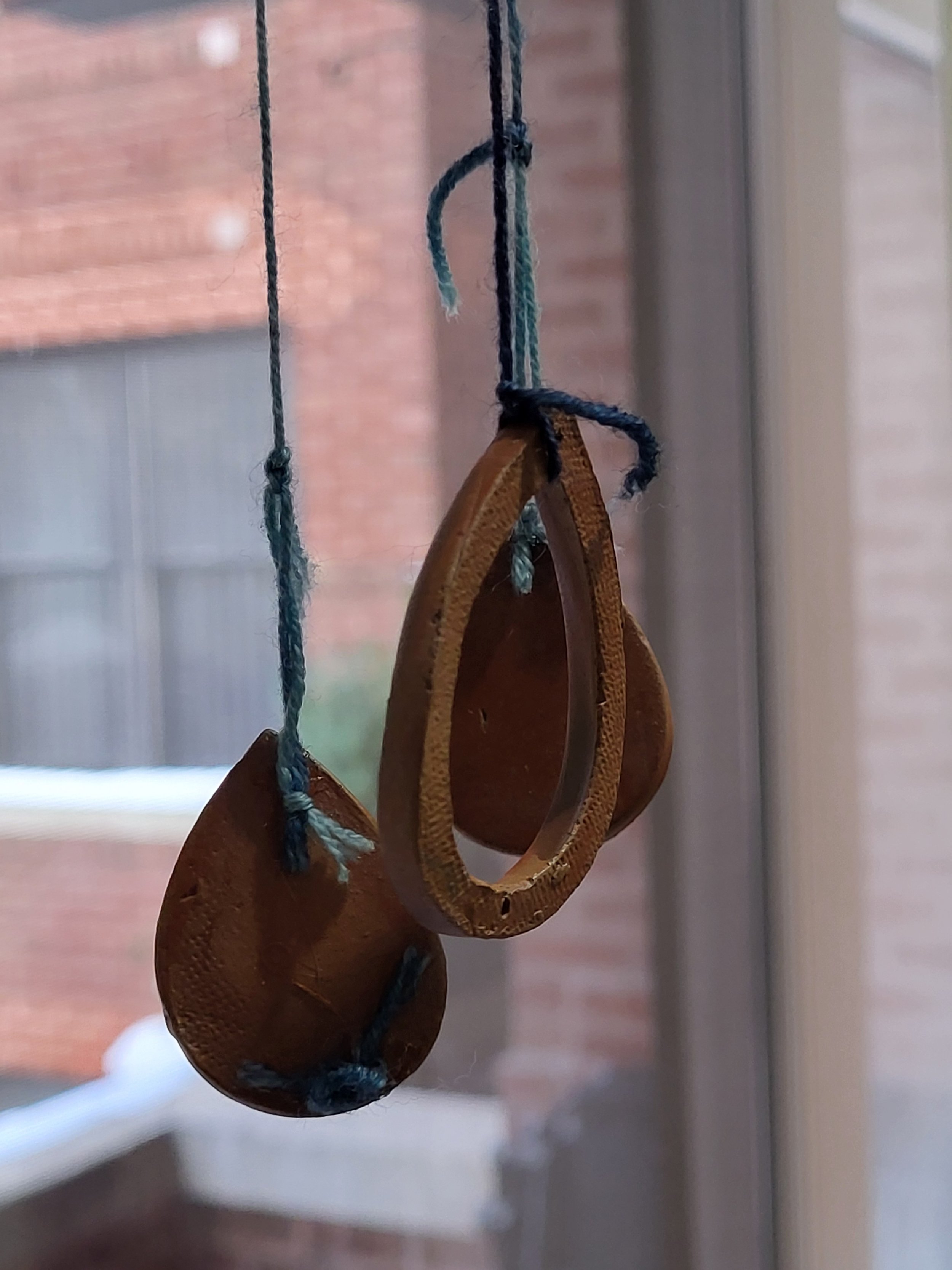 Terracotta shapes hang on blue yarn in front of a window